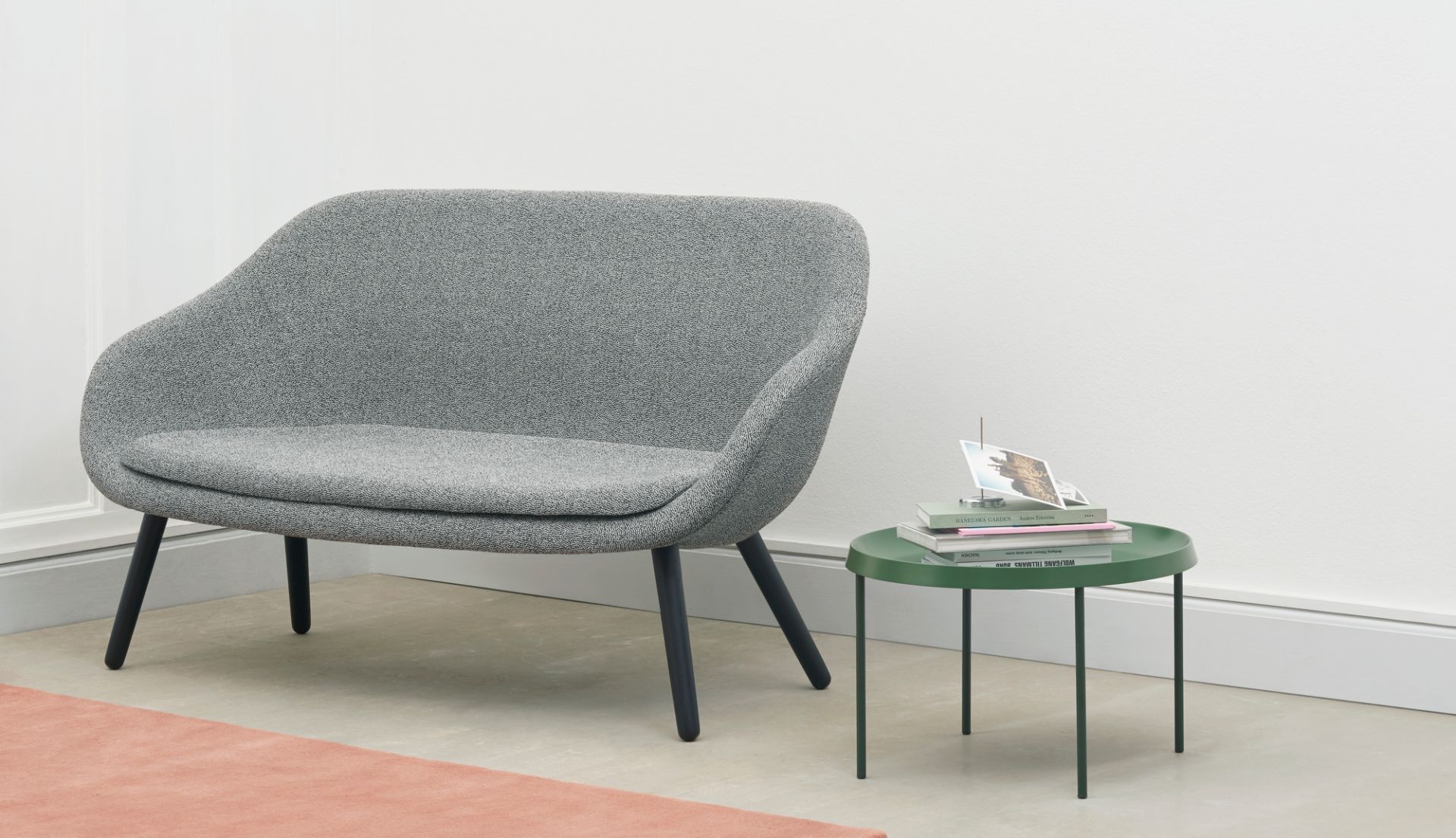 Graues About a Lounge Sofa von Hay mit schwarzem Gestell neben grünem Beistelltisch.