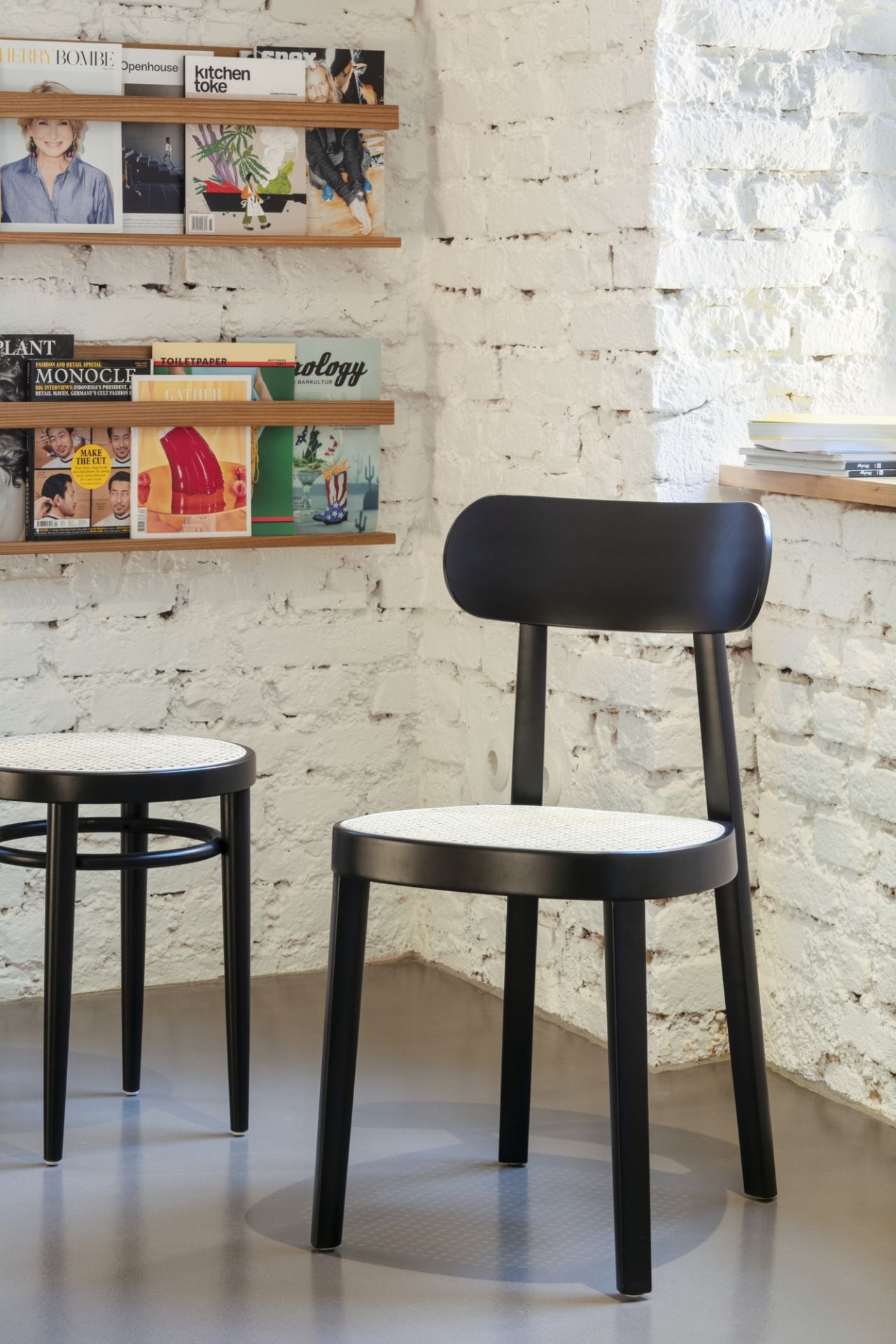 Schwarzer Holzstuhl, Modell 118, von Thonet mit Wiener Geflecht Sitzfläche vor einer weißen Ziegelwand.