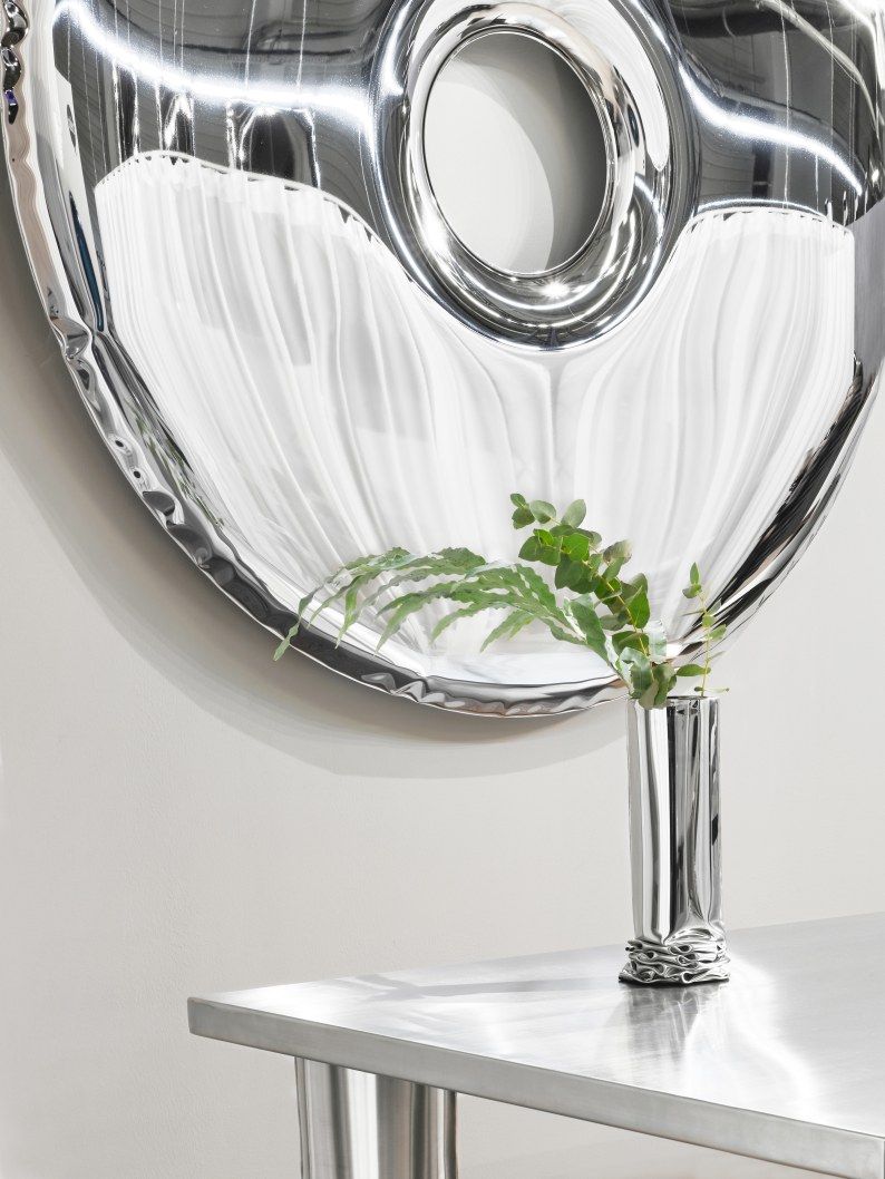 Detailaufnahme: Moderner Crash Table Esstisch Zieta aus poliertem Stahl mit passender Vase und Pflanze.