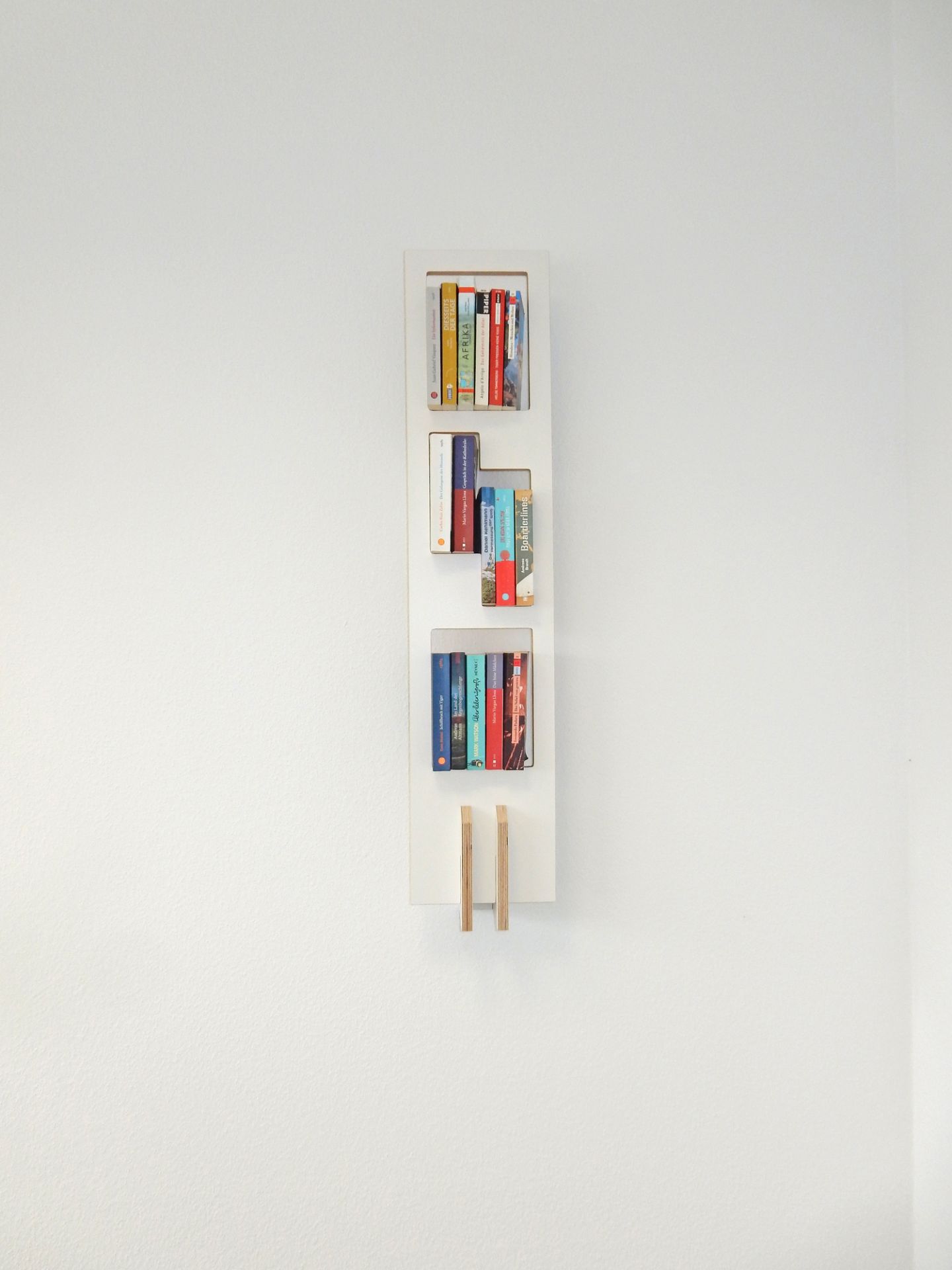 Weißes Tojo Lesestoff Bücherregal an einer weißen Wand mit bunten Büchern gefüllt.