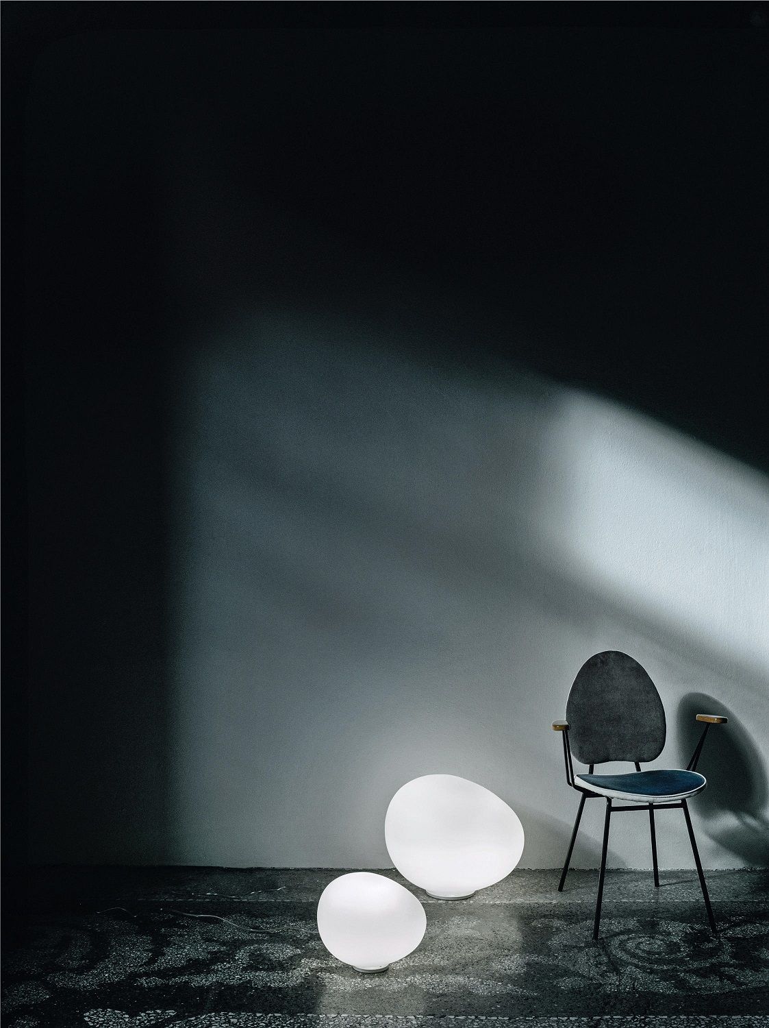 Zwei Gregg Bodenleuchten von Foscarini neben einem Stuhl, stimmungsvolle Beleuchtung für den Außenbereich.