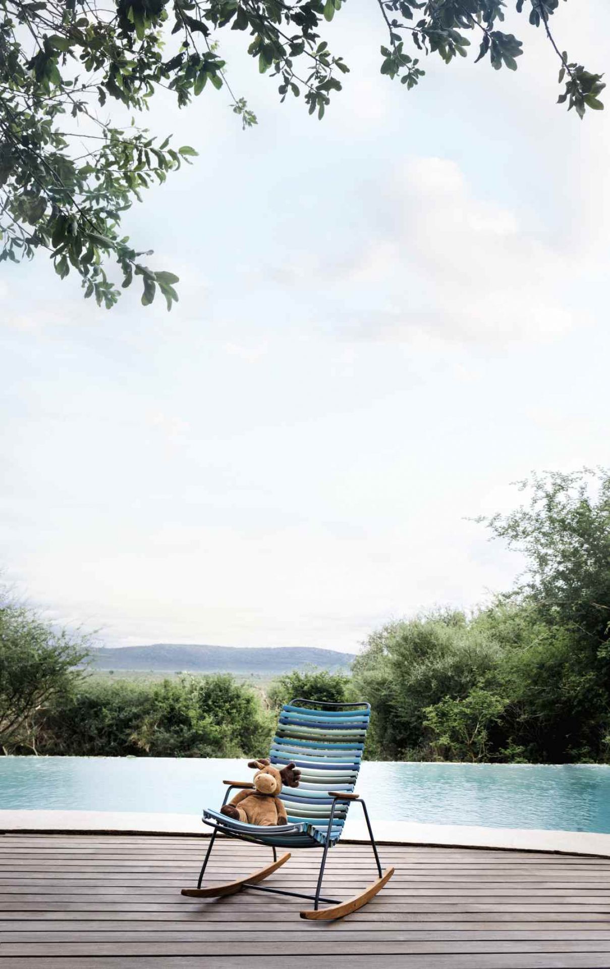 Click Schaukelstuhl Outdoor von Houe mit blau-grünen Streifen und Stofftier am Pool.