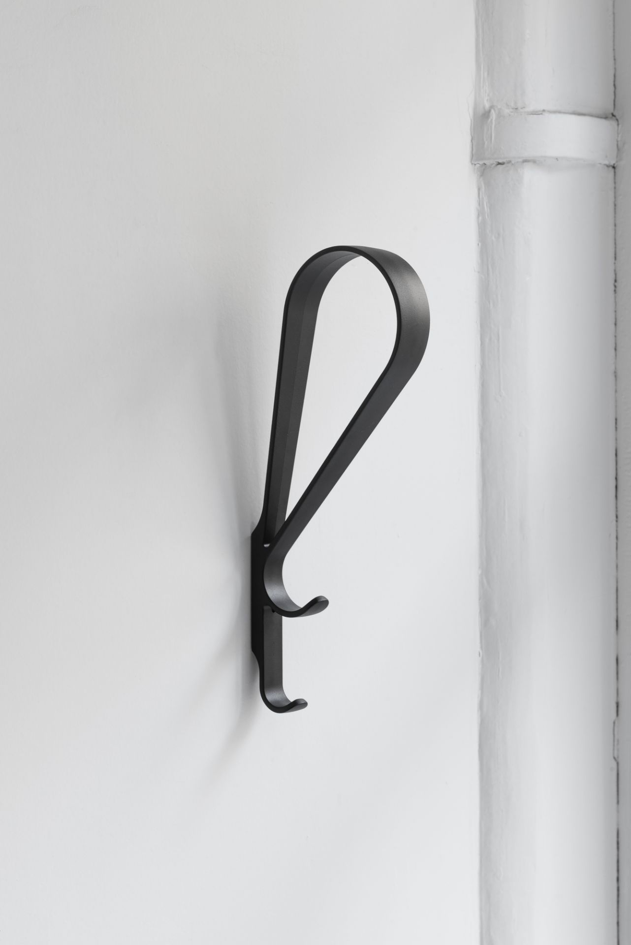 Schwarzer Artek Tupla Wandhaken an einer weißen Wand, minimalistisches Design für Garderobe oder Bad.