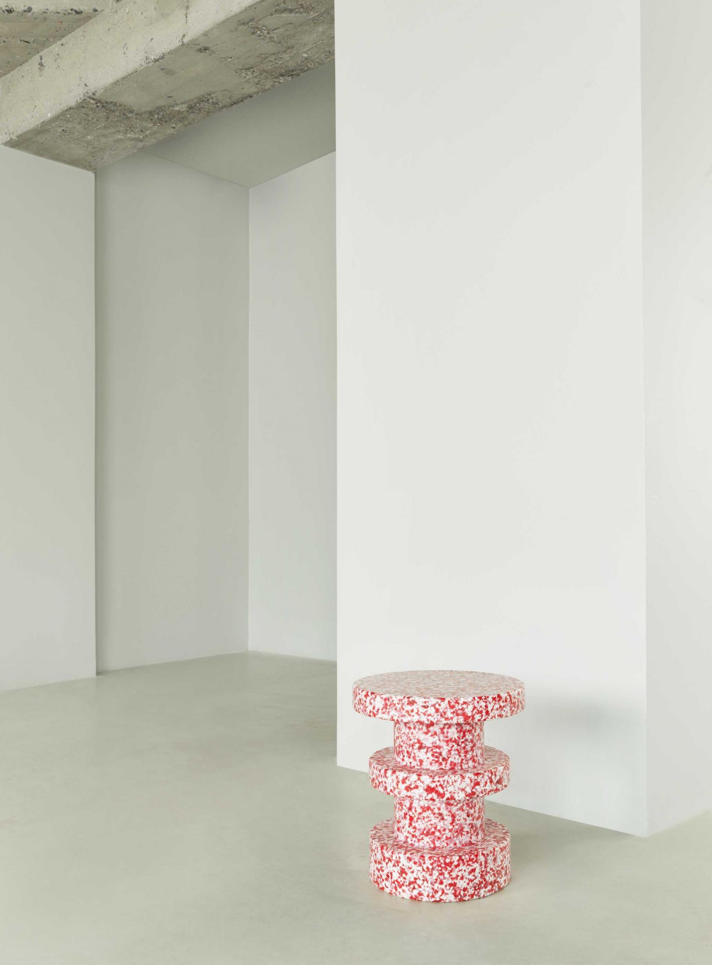 Normann Copenhagen Bit Stool Stack Hocker in Rot-Weiß gesprenkelt vor weißer Wand im minimalistischen Raum.