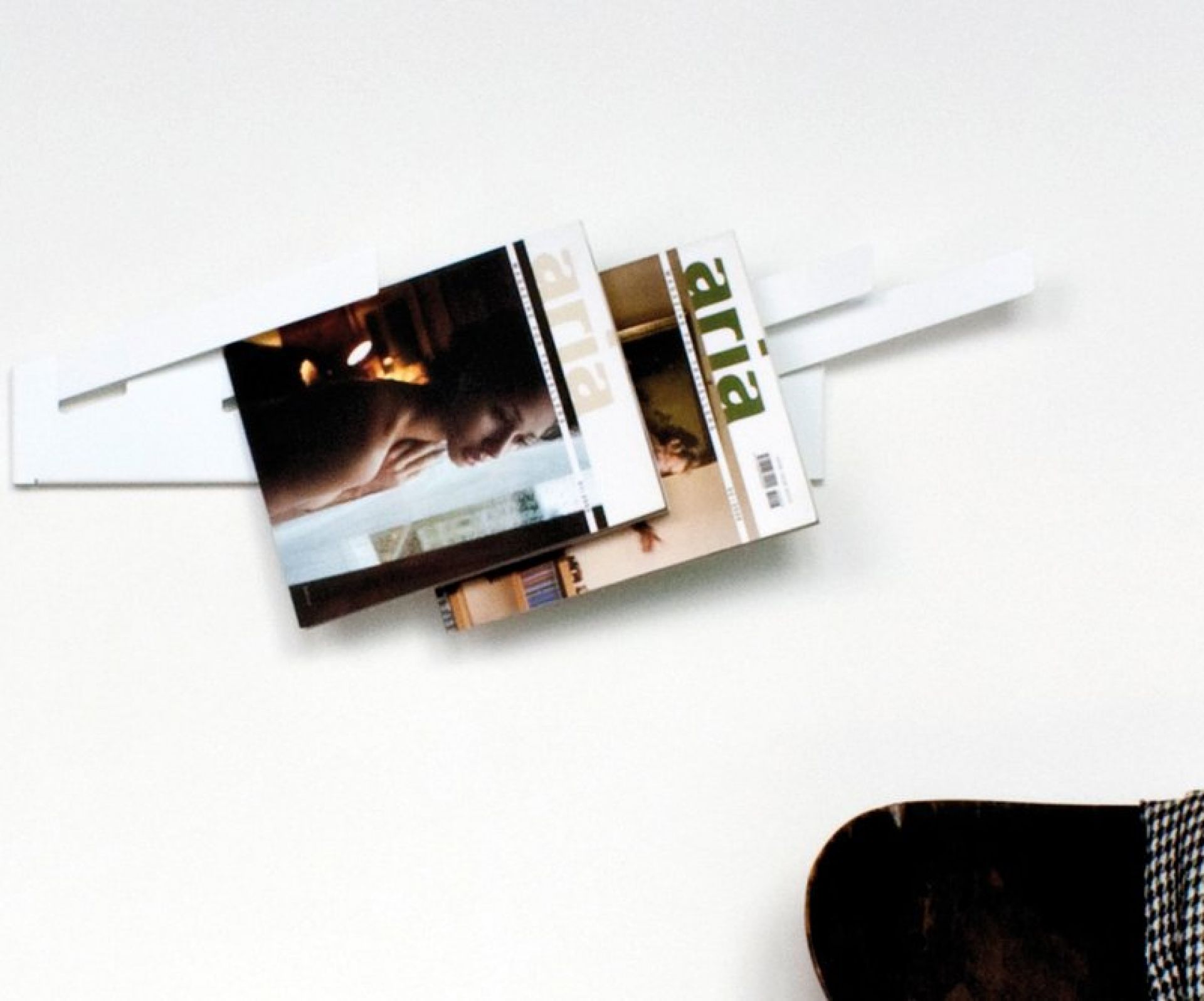 Wandmontierter Magazinständer aus weißem Metall mit zwei Zeitschriften der Marke "aria" in einem minimalistischen Design.
