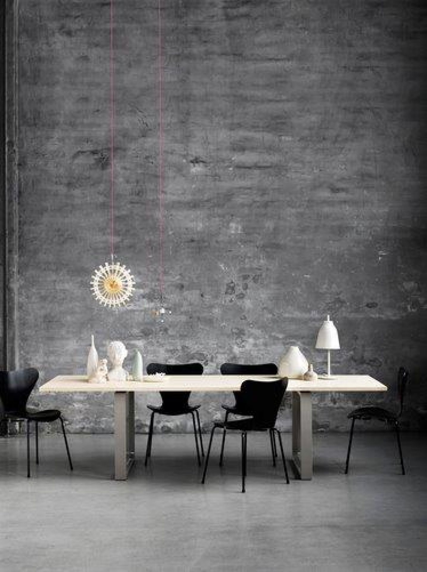 Fritz Hansen Essay Tisch mit Stühlen und Dekoration vor einer grauen Wand.