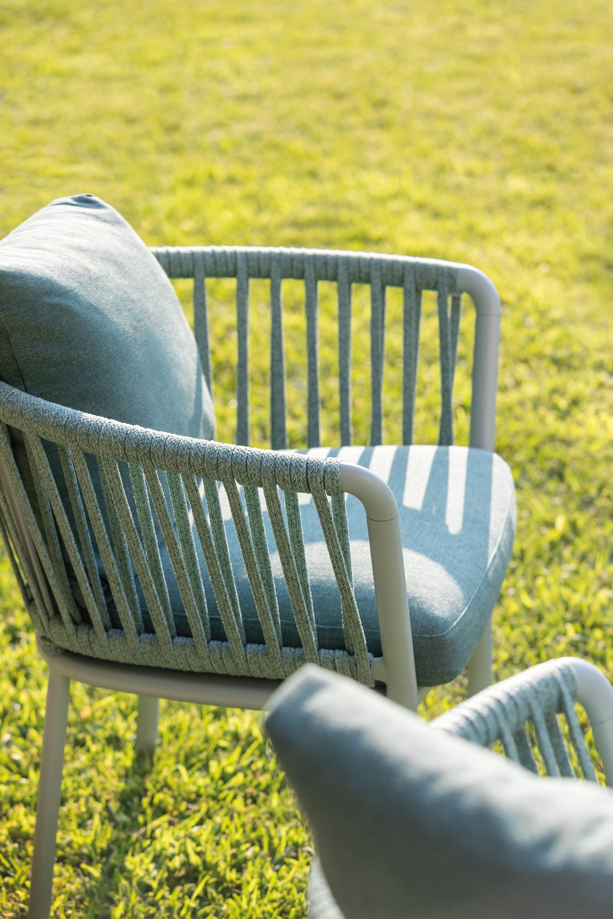 Detailaufnahme: Moderner Ria Stuhl mit hellgrauem Gestell und geflochtener Rückenlehne im Garten.