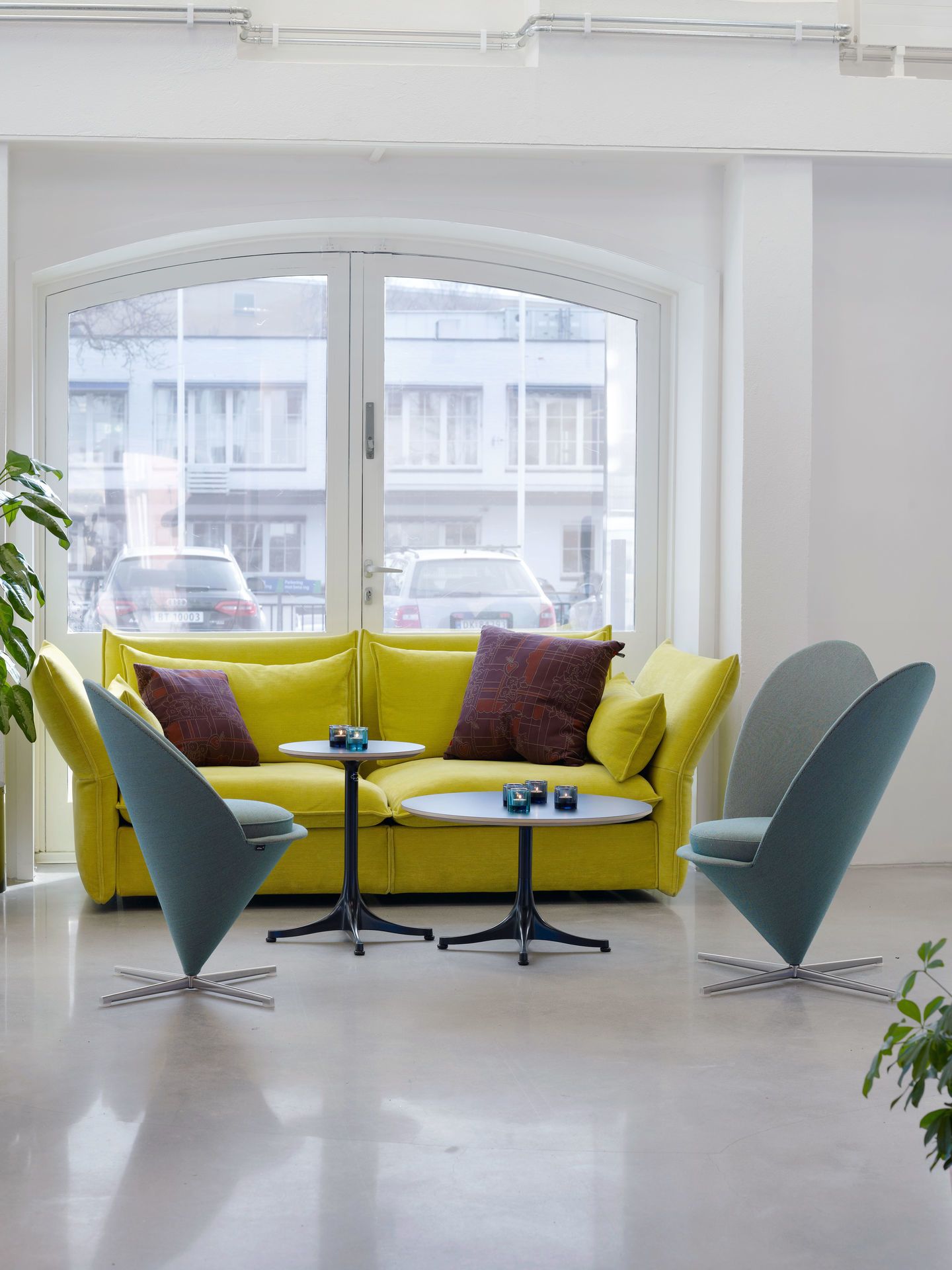 Innenaufnahme mit gelbem Sofa, zwei Heart Cone Chairs von Vitra und kleinen Tischen.