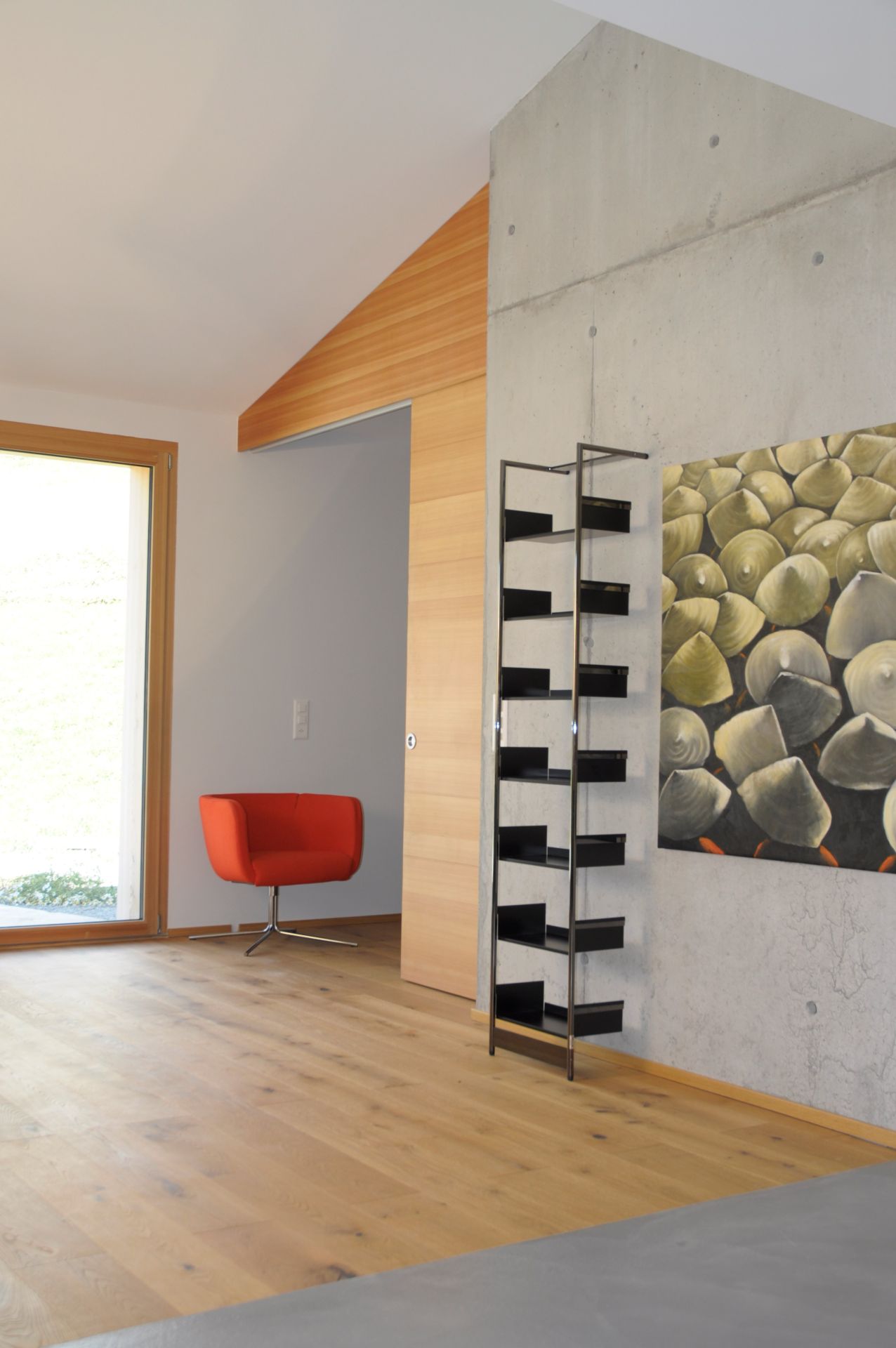Modernes Wohnzimmer mit Pool 196 Anlehnregal von Mox, rotem Sessel und Kunstwerk an der Betonwand.