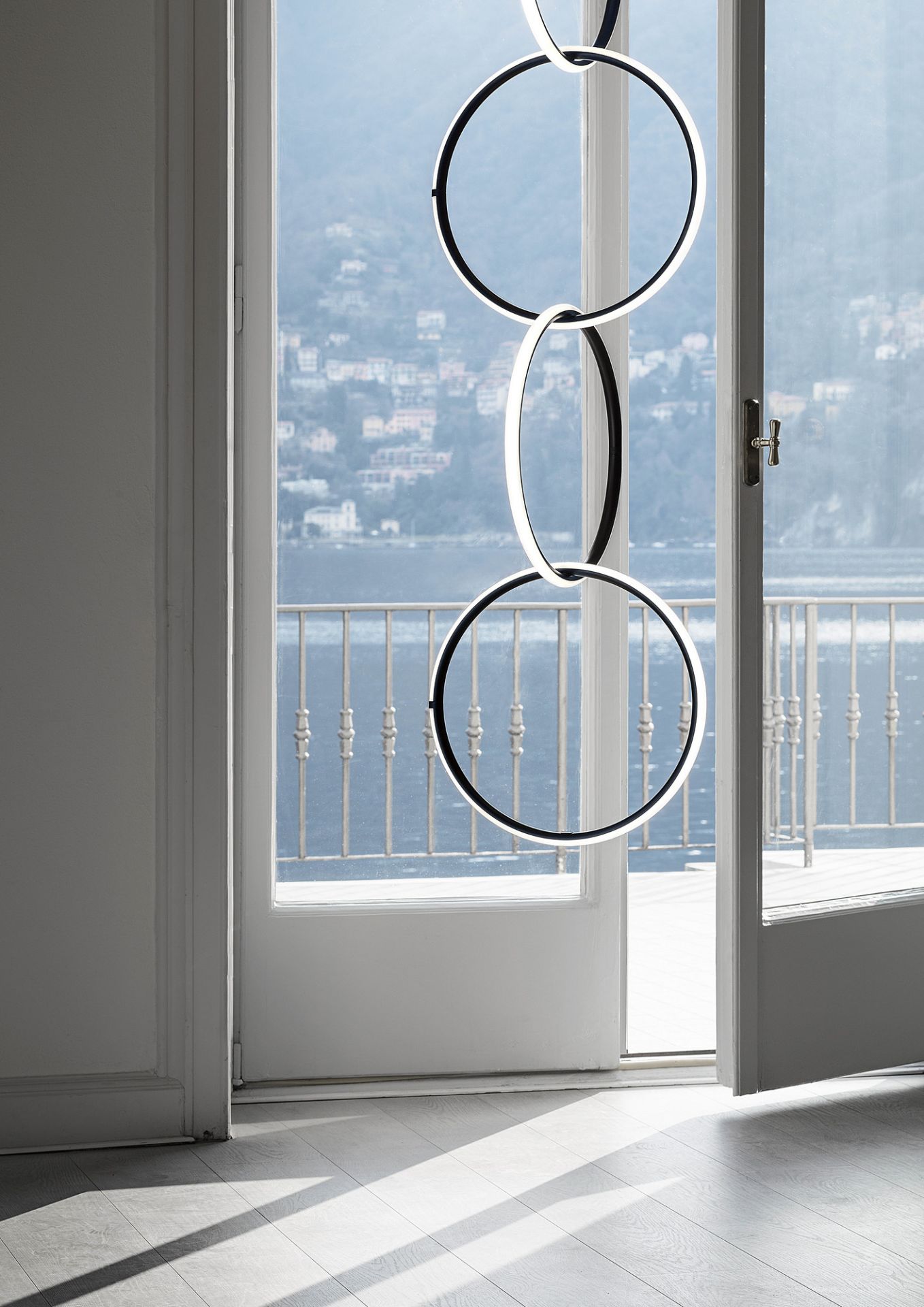 Moderne Arrangements Pendelleuchte von Flos mit drei ineinandergreifenden, leuchtenden Ringen vor einer offenen Balkontür.