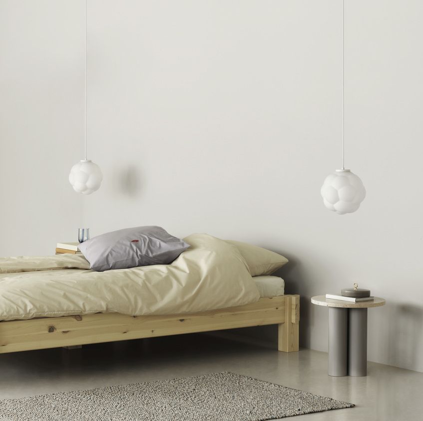 Normann Copenhagen Dit Coffee Table Beistelltisch neben einem Bett mit Lampe und Teppich im Schlafzimmer.
