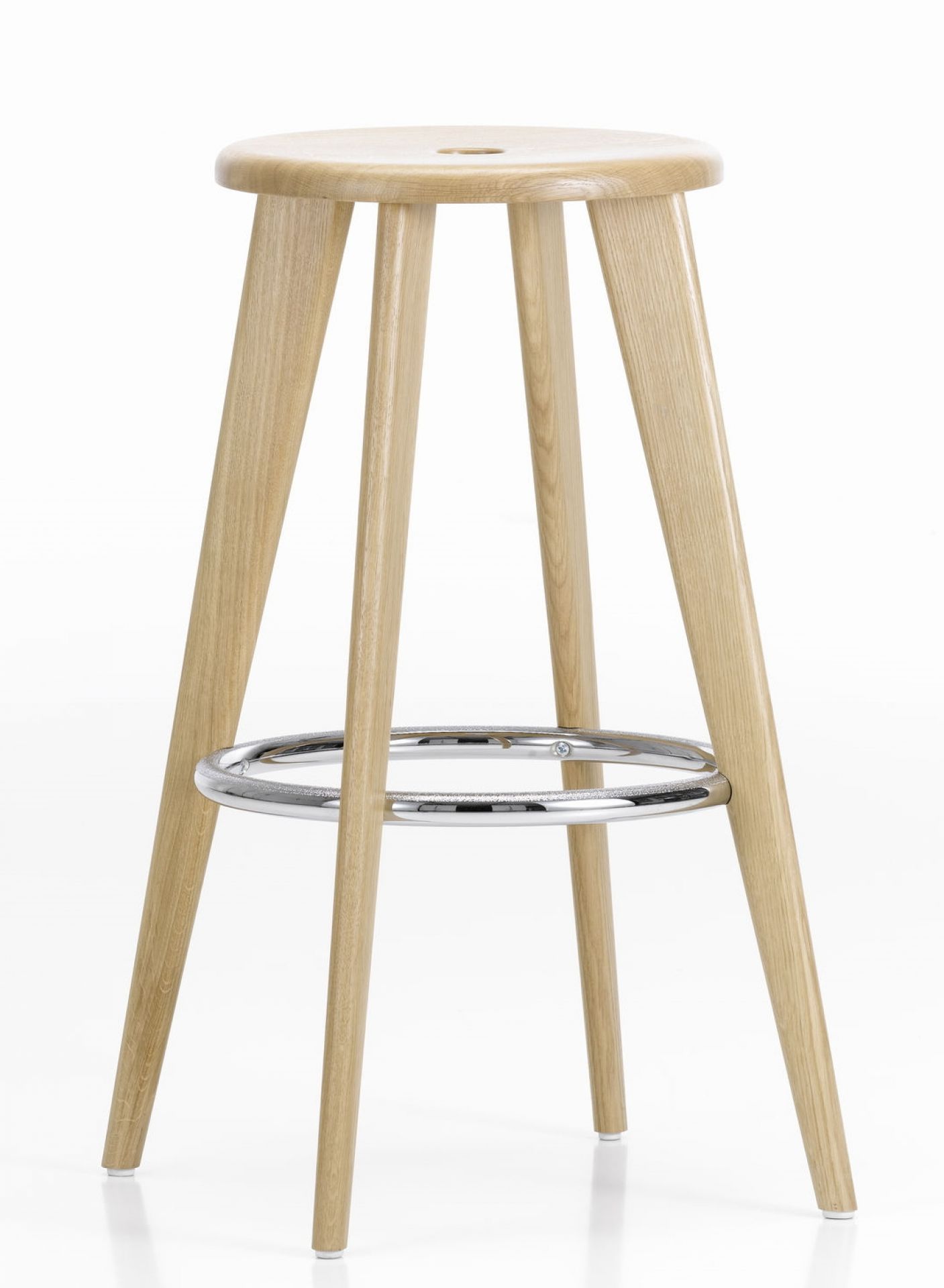 Vitra Tabouret Haut Barhocker aus Eiche natur mit Fußstütze aus Chrom vor weißem Hintergrund.