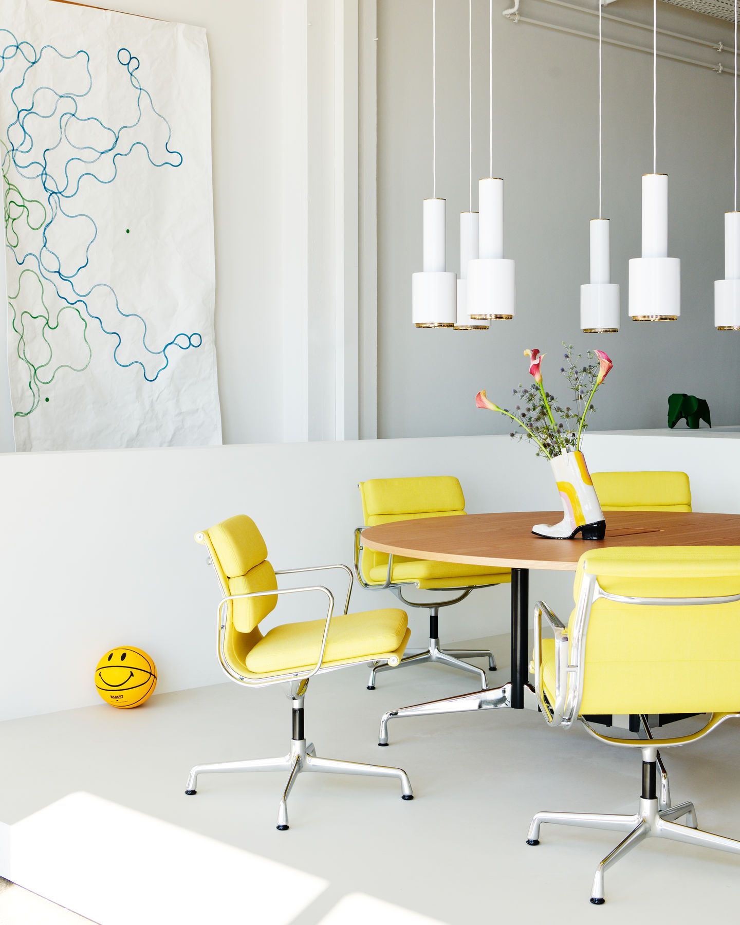 Gelbe Vitra Soft Pad Chairs EA207 um einen Holztisch in einem hellen, modernen Raum.
