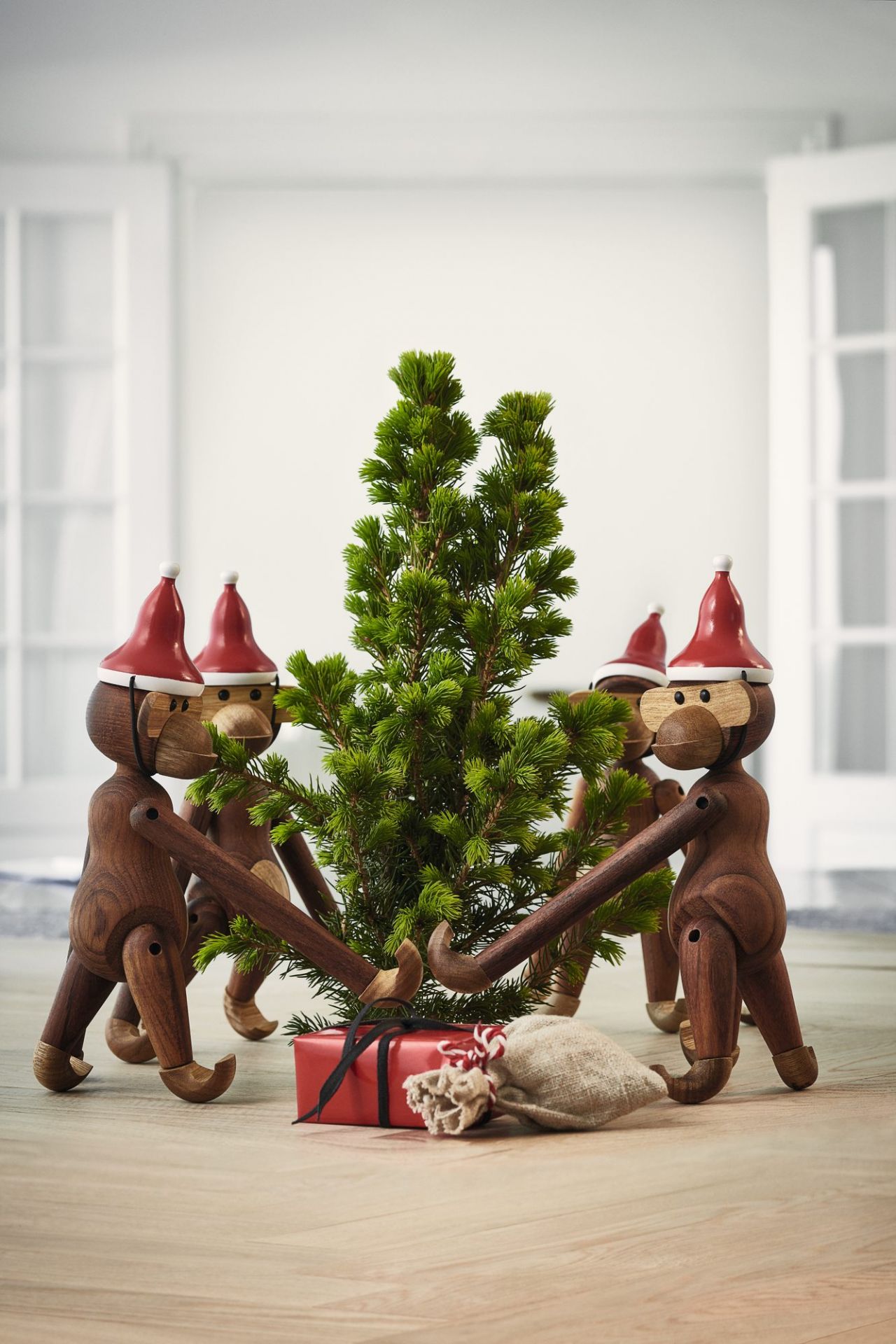 Kay Bojesen Affen mit Weihnachtsmütze um einen kleinen Weihnachtsbaum, Geschenke liegen darunter, festliche Dekoration.