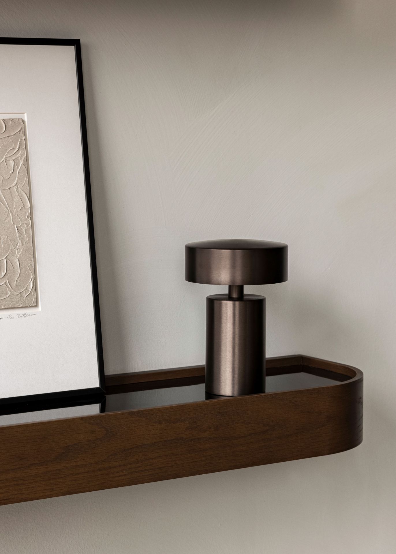 Nahaufnahme der Audo Column Tischleuchte in Bronze auf einem Holzregal. Tragbare Lampe.