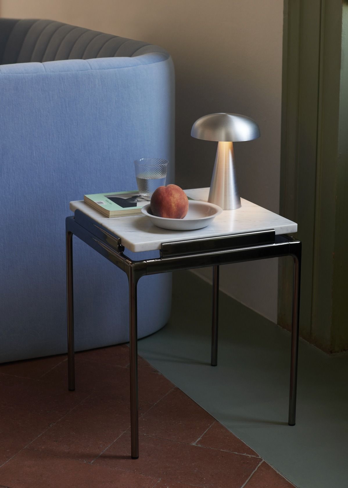 AndTradition Sett LN11 Beistelltisch mit Marmorplatte, Lampe, Pfirsich und Glas Wasser neben blauem Sofa.