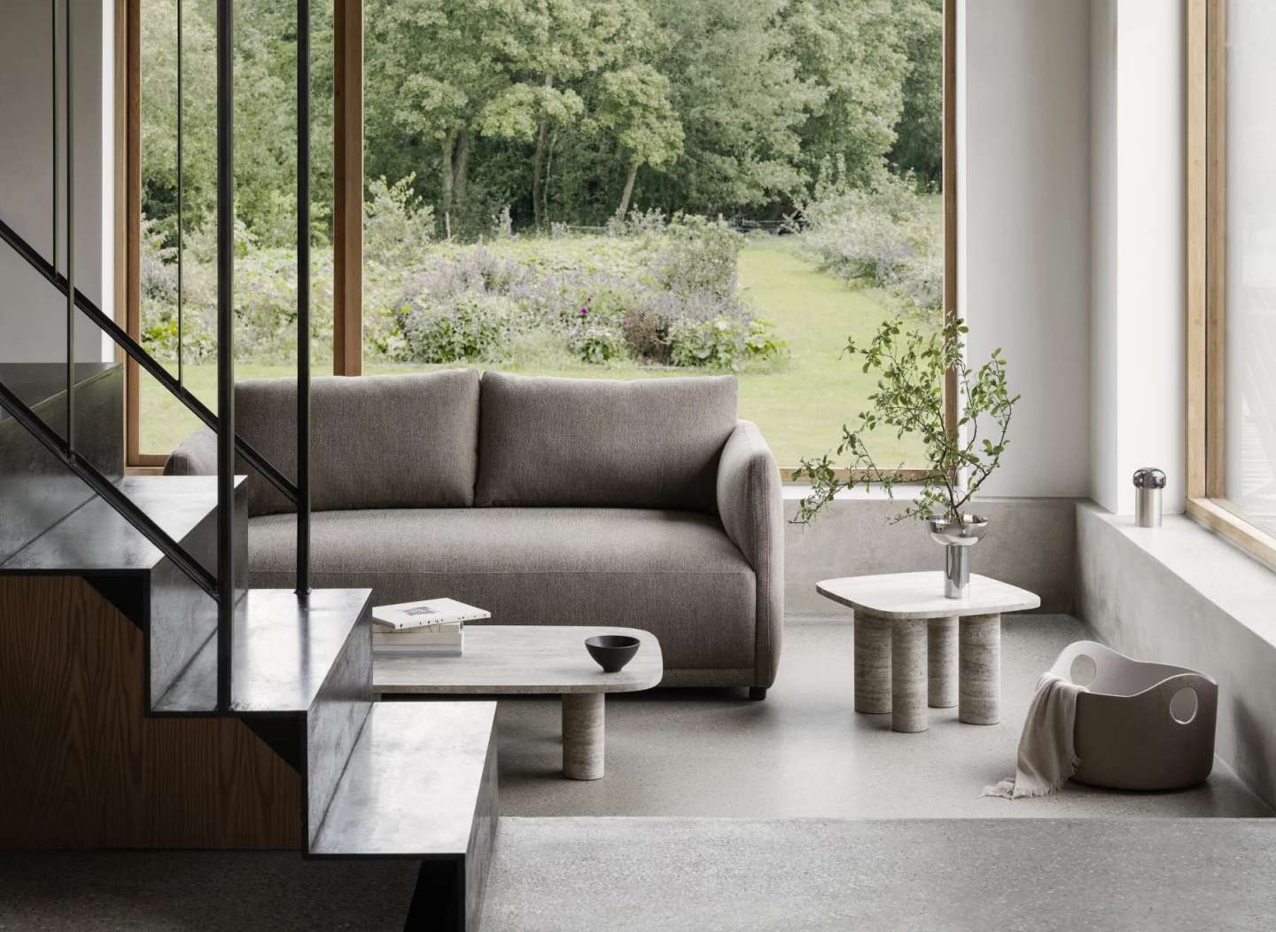 Moderner Wohnraum mit Blomus Volos Beistelltisch aus Travertin, quadratische Tischplatte und zylindrischen Beinen, neben grauer Couch.