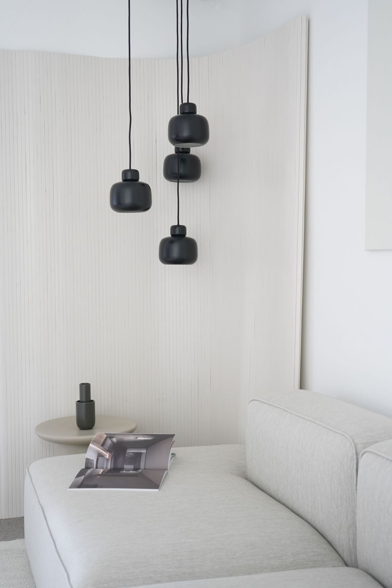 Nahaufnahme von drei kleinen, schwarzen Stone Pendant Pendelleuchten von Woud über einem hellen Sofa.