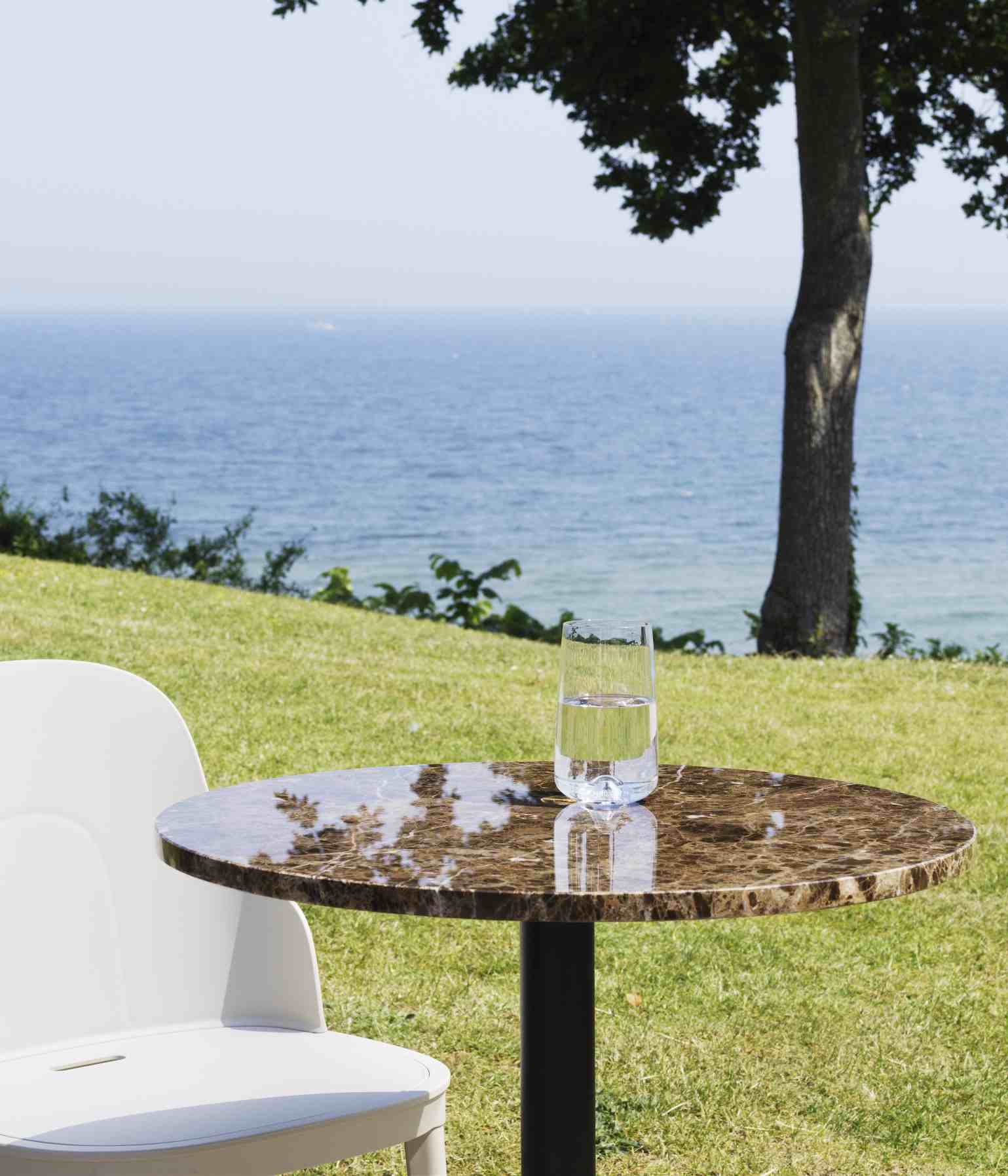 Allez Chair von Normann Copenhagen, weißer Stuhl mit Tisch und Meerblick im Hintergrund.