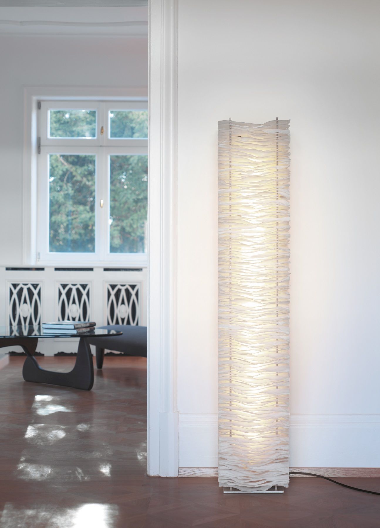 Moderne weiße Stehlampe mit gewelltem Lampenschirm im minimalistischen Wohnzimmer für stimmungsvolle Beleuchtung.