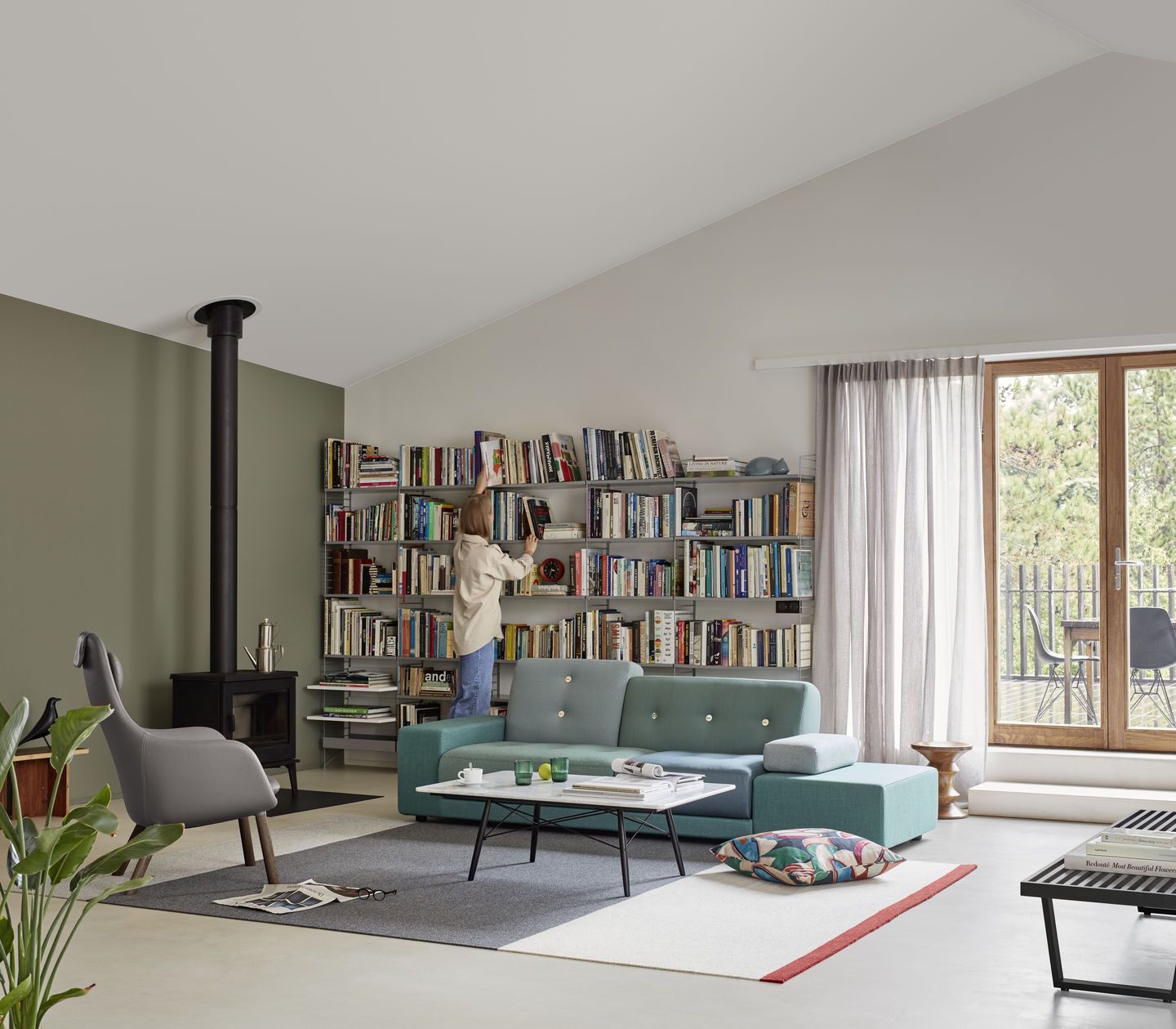 Helles Wohnzimmer mit mintgrünem Polder Sofa von Vitra, Bücherregal und Person, die ein Buch entnimmt.
