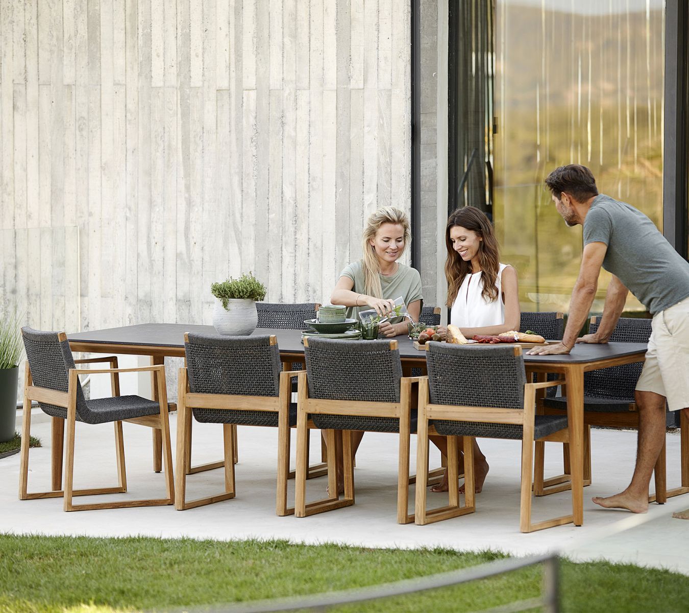 Endless Sessel von Cane-Line am Gartentisch mit Personen, moderne Gartenmöbel aus Teakholz und Geflecht.