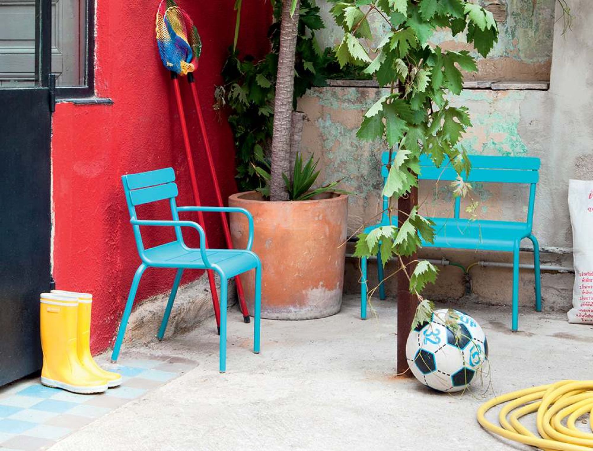 Fermob Luxembourg Kinderbank in Türkis im Garten mit Spielzeug und Pflanzen.