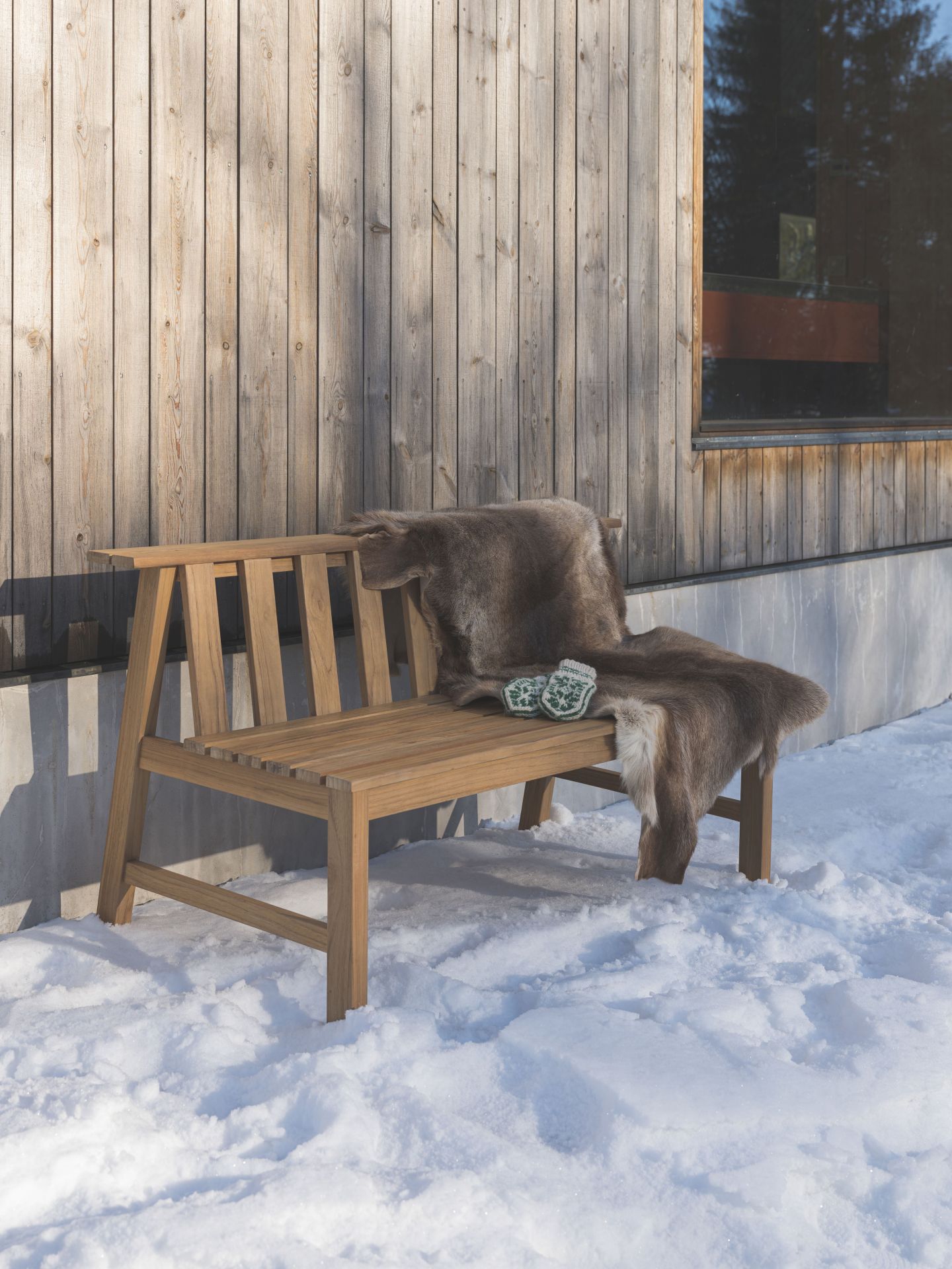Cadence Bank Teakholz Gartenbank von Fritz Hansen mit Fell und Strickhandschuhen im Schnee.