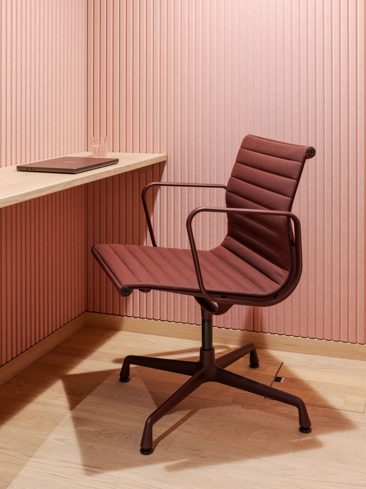 Nahaufnahme eines burgunderroten Vitra EA 108 Aluminium Chair Bürostuhls mit Armlehnen vor rosa Wand.