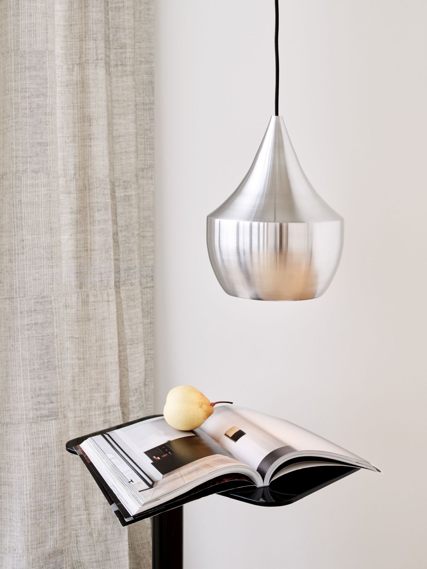 Nahaufnahme der Tom Dixon Fat Pendelleuchte aus gebürstetem Stahl, hängend über einem Magazin mit Birne.