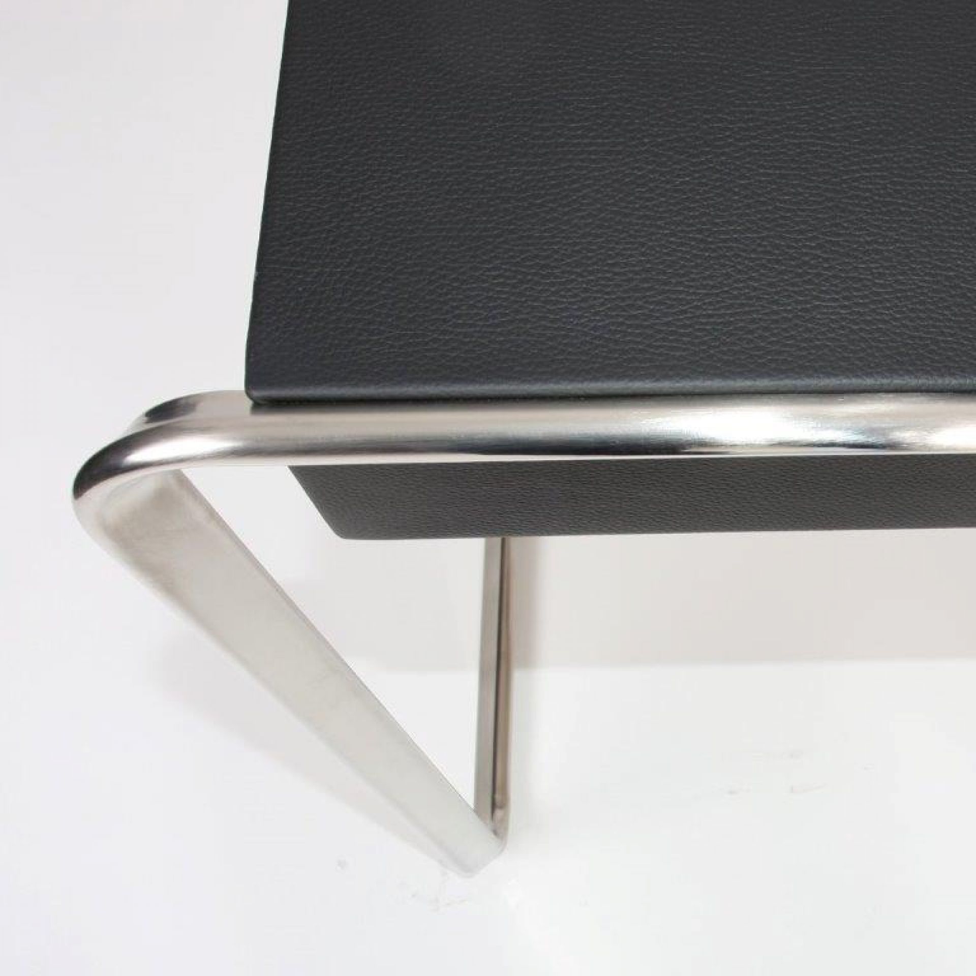 Detailaufnahme eines schwarzen Lederstuhls mit verchromtem Stahlrohrgestell, modernes Möbeldesign.