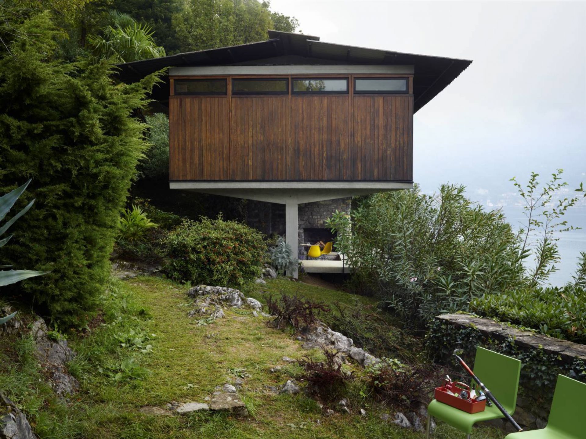 Rote Vitra Toolbox auf grünem Stuhl vor modernem Haus am Hang mit Seeblick.