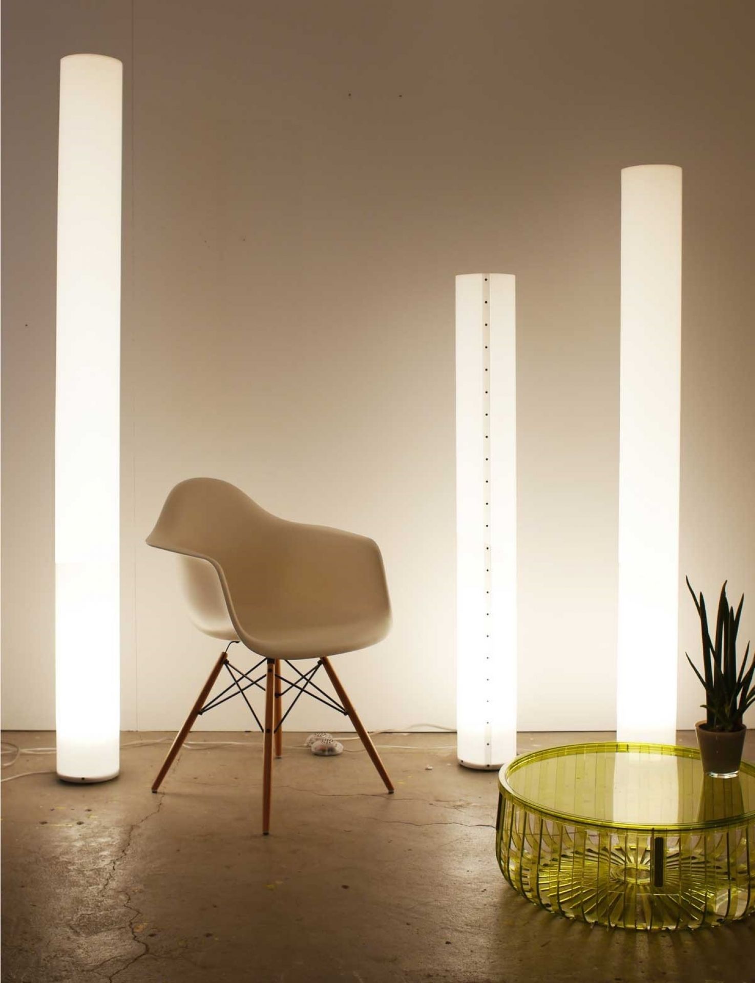 Drei leuchtende, weiße LED Stehlampen, darunter die Chameledeon XL, mit Stuhl und Beistelltisch.