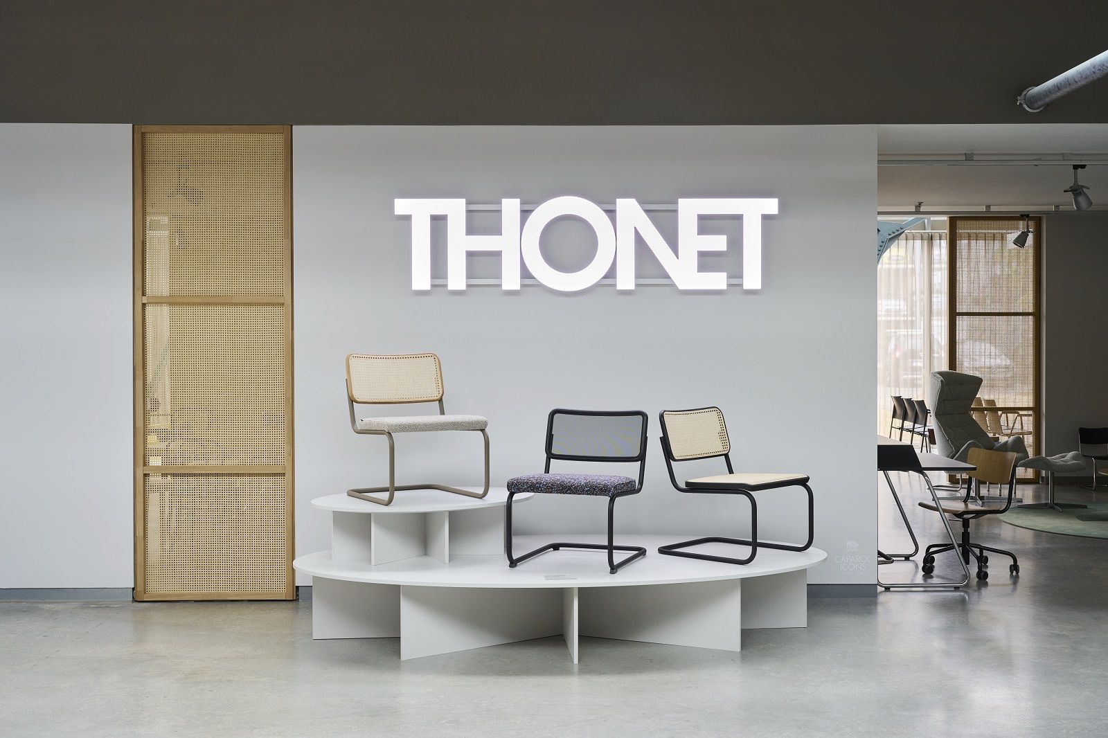 Ausstellung mit drei verschiedenen Thonet S 32 VL Lounge Chair Sesseln auf einem weißen Podest vor Thonet Logo.
