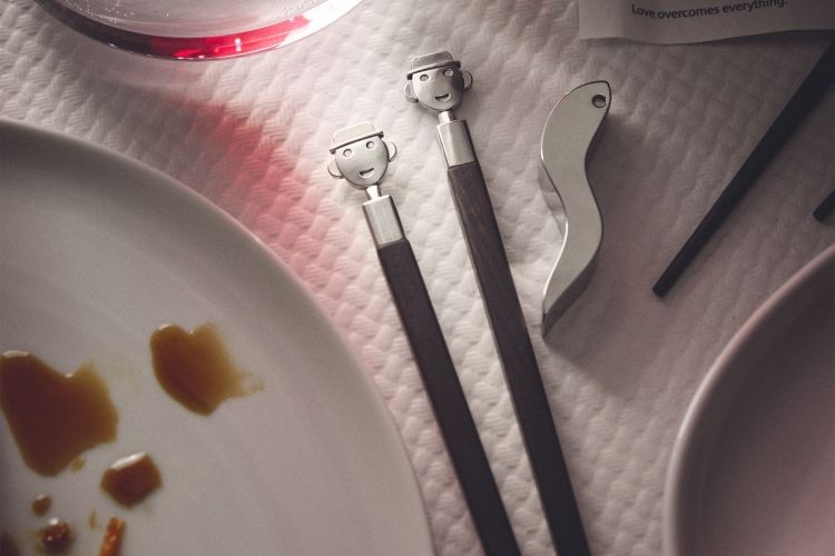 Alessi Anna Stick AM44SET2 Essstäbchen-Set mit lustigen Gesichtern, Essensreste auf Tellern und Besteck.