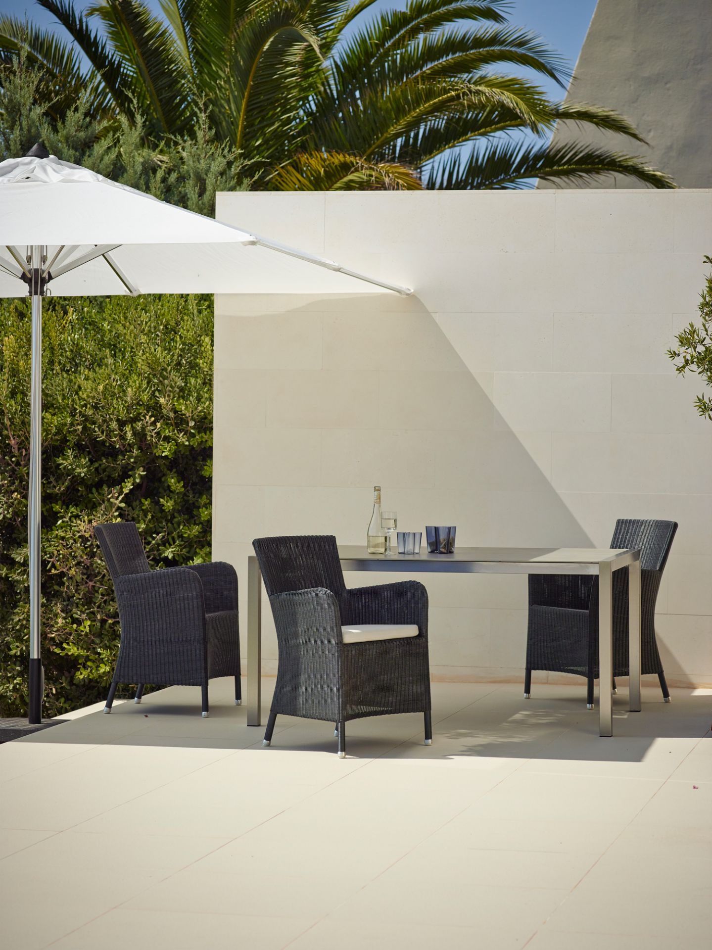 Hampsted Cane-Line Outdoor Sessel aus Rattan mit Tisch und Sonnenschirm auf einer Terrasse.
