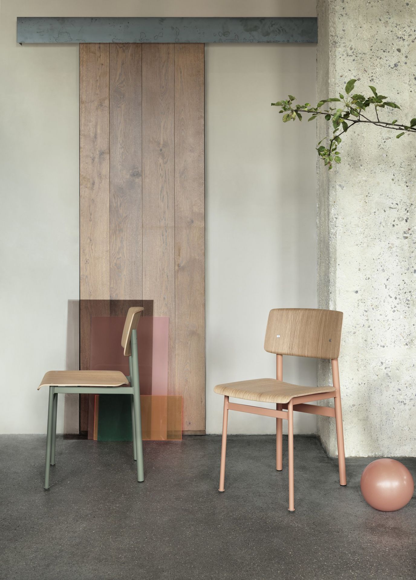 Zwei Muuto Loft Chair Stühle in Grün und Rosa vor Holztür und Betonwand.
