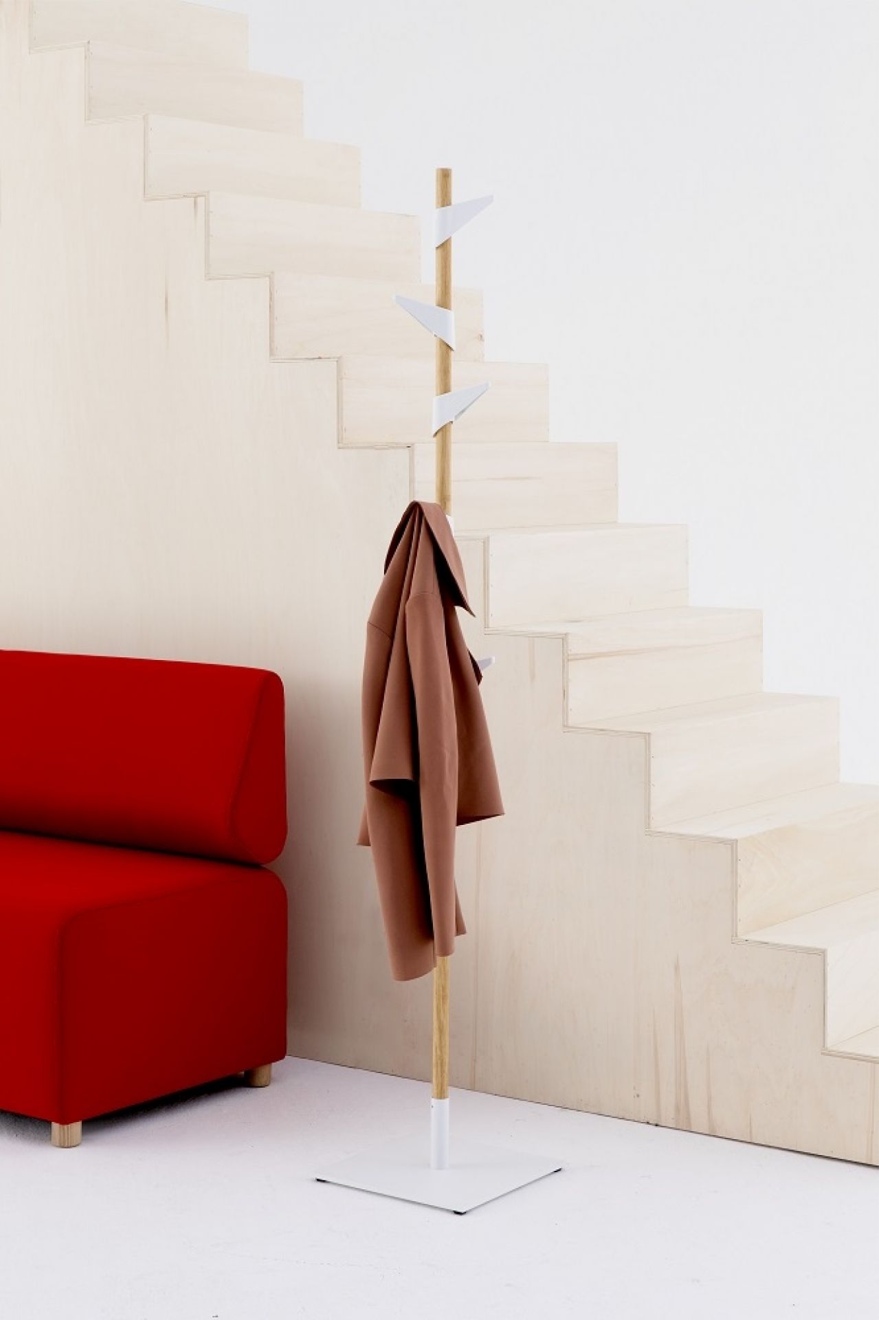 Cascando Standgarderobe aus Bambus mit Mantel vor Treppe und rotem Sofa im minimalistischen Design.
