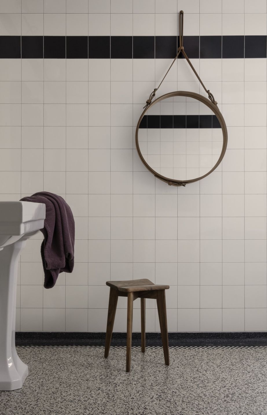 Adnet Circular Wandspiegel von Gubi im Badezimmer mit Fliesen, Waschbecken und Holzhocker.