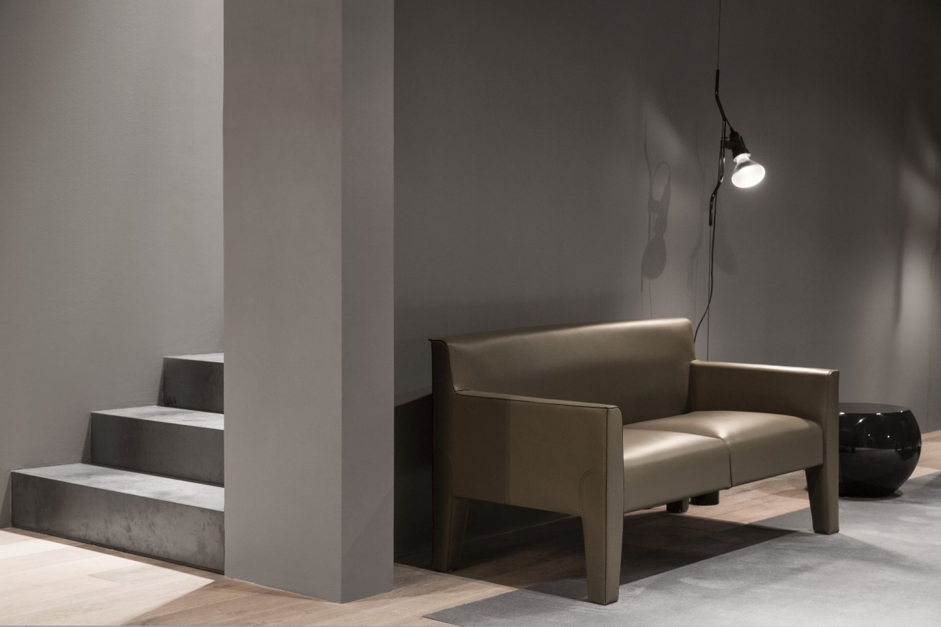 Innenaufnahme mit Flos Parentesi D Lampe, weiß, neben modernem Sofa und Treppe.