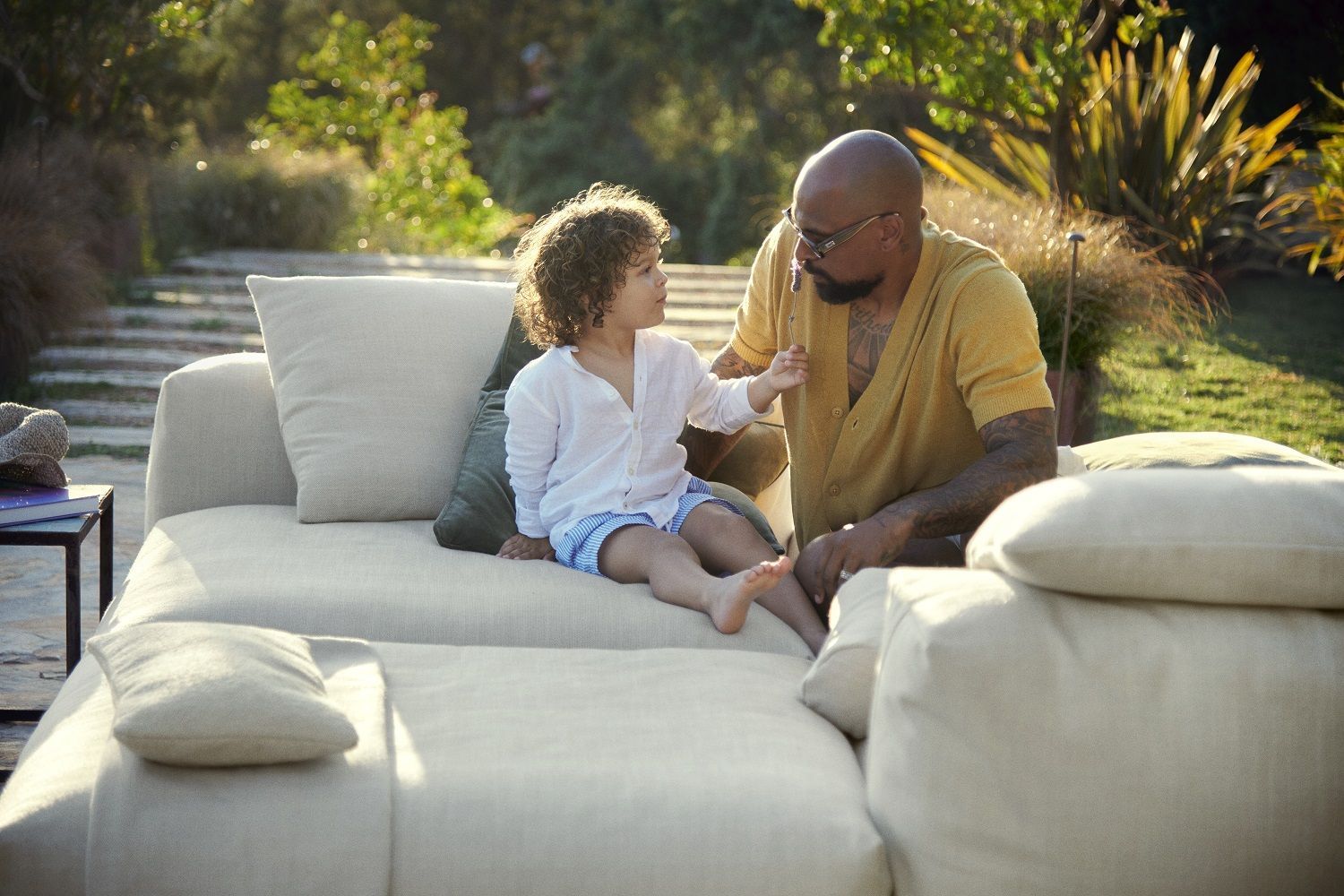 Vater und Kind entspannen auf dem beigen vetsak Noodle Pillow Pique Outdoor Kissen im Garten.