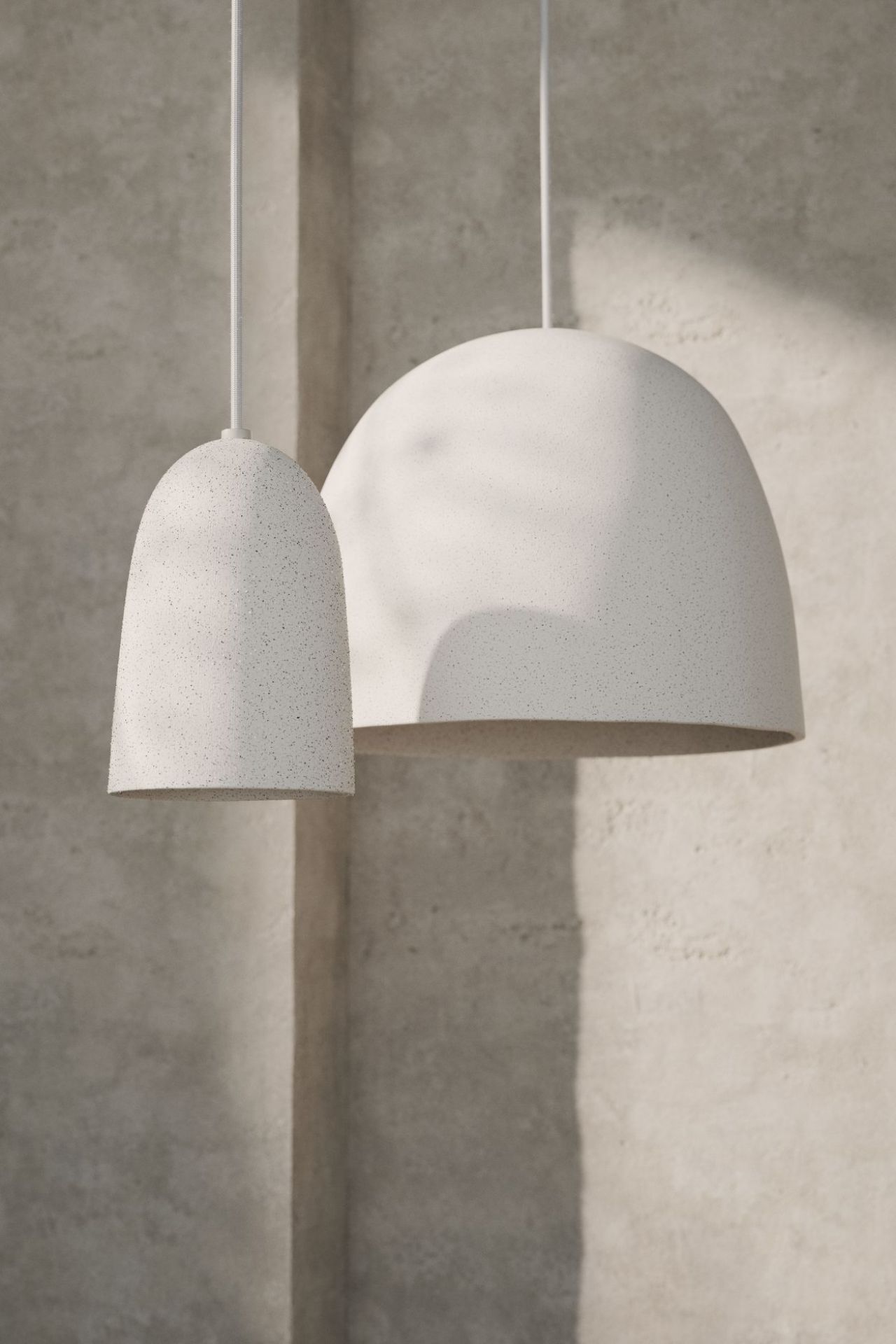 Zwei weiße Speckle Pendelleuchten von Ferm Living in unterschiedlichen Größen hängen vor einer Wand.