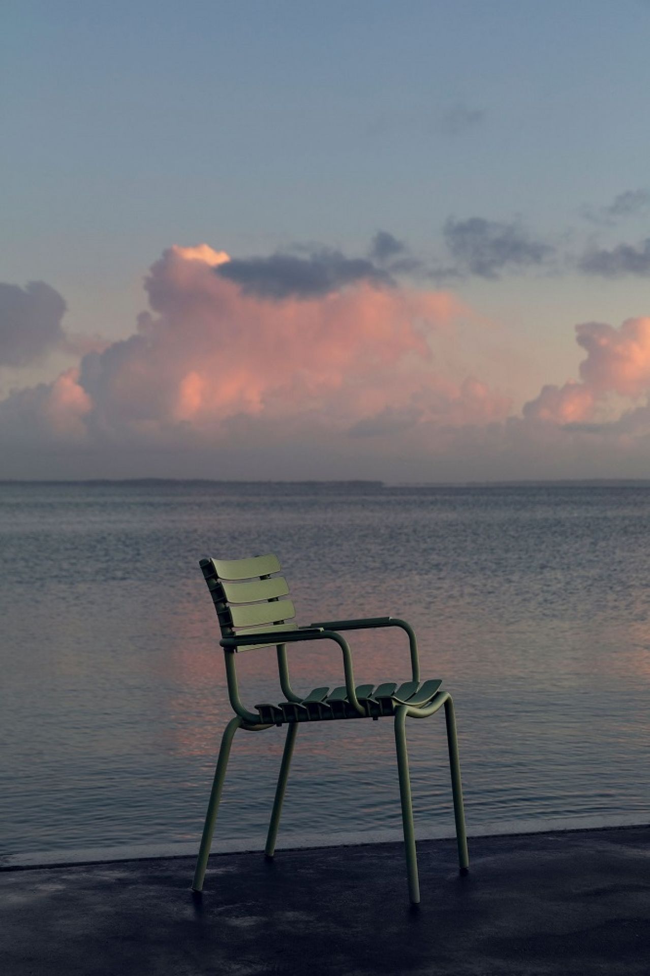 Grüner Houe ReClips Stuhl für den Außenbereich vor einem ruhigen Meer bei Sonnenuntergang.