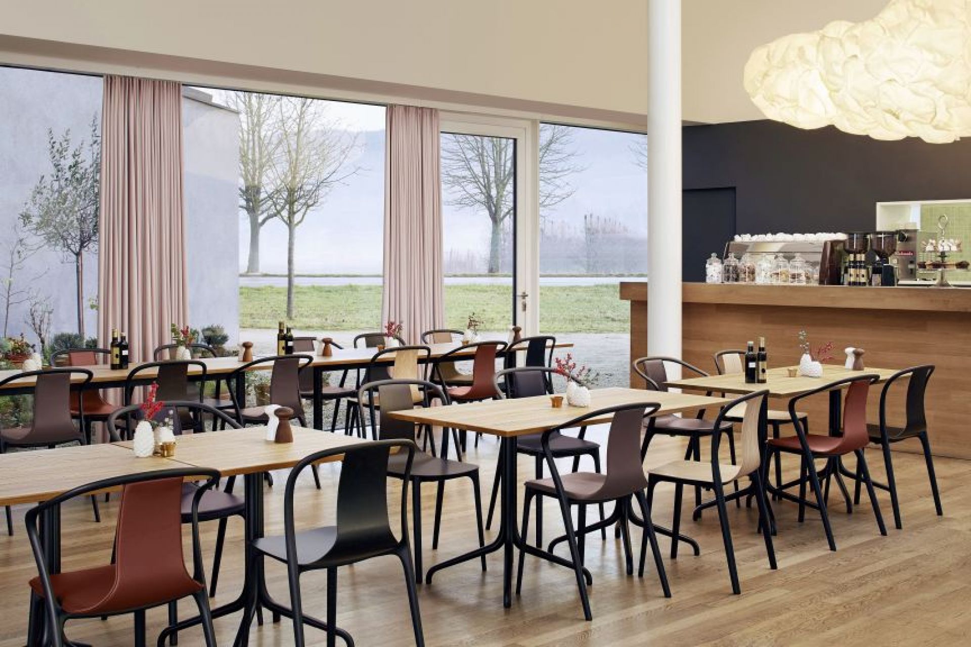 Innenansicht eines Restaurants mit mehreren Vitra Belleville Tischen und Stühlen mit Holzboden und großen Fenstern.
