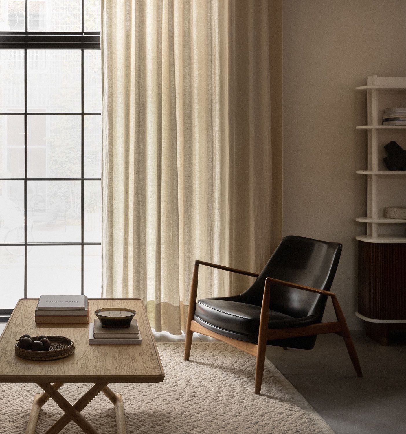 Beiger Audo Copenhagen Gravel Rug Teppich in einem Wohnzimmer mit Sessel und Holztisch.