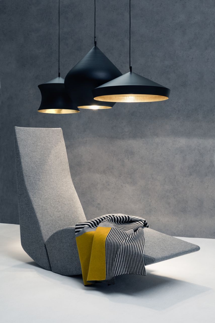 Drei schwarze Beat Pendelleuchten von Tom Dixon über einem grauen Sessel mit Decke.