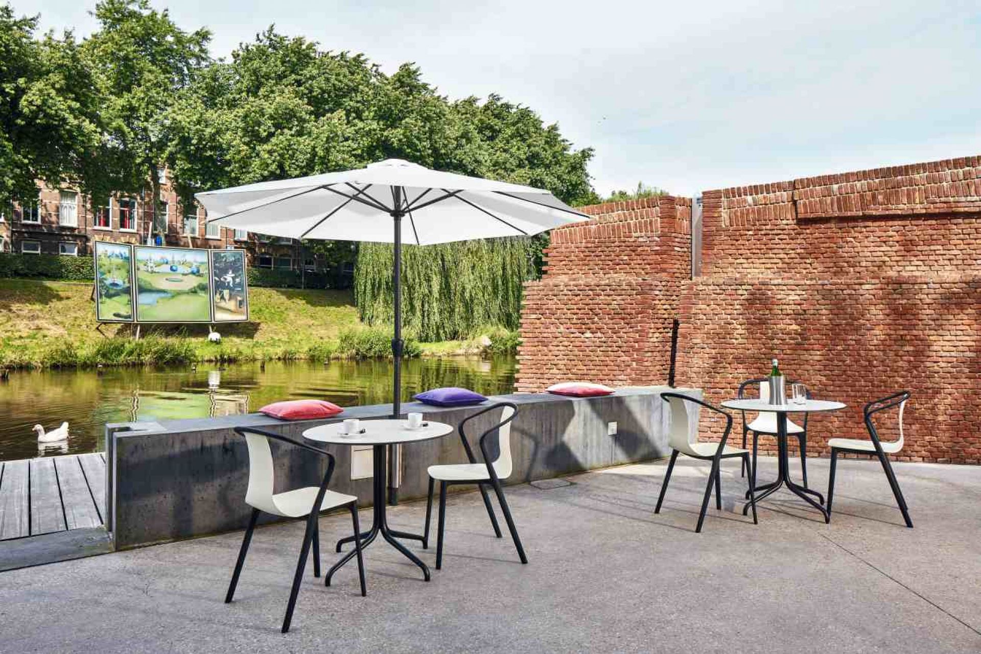 Vitra Bistro Table, runder Gartentisch mit Sonnenschirm und Stühlen im Außenbereich am Wasser.