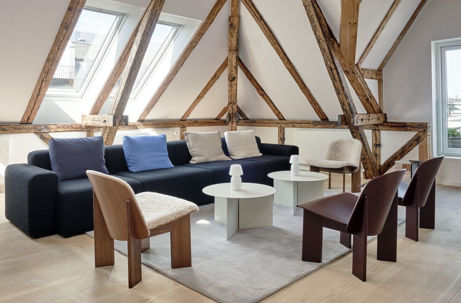 Wohnzimmer mit Hay Chisel Lounge Chairs aus Holz und schwarzem Sofa unter Dachschrägen.