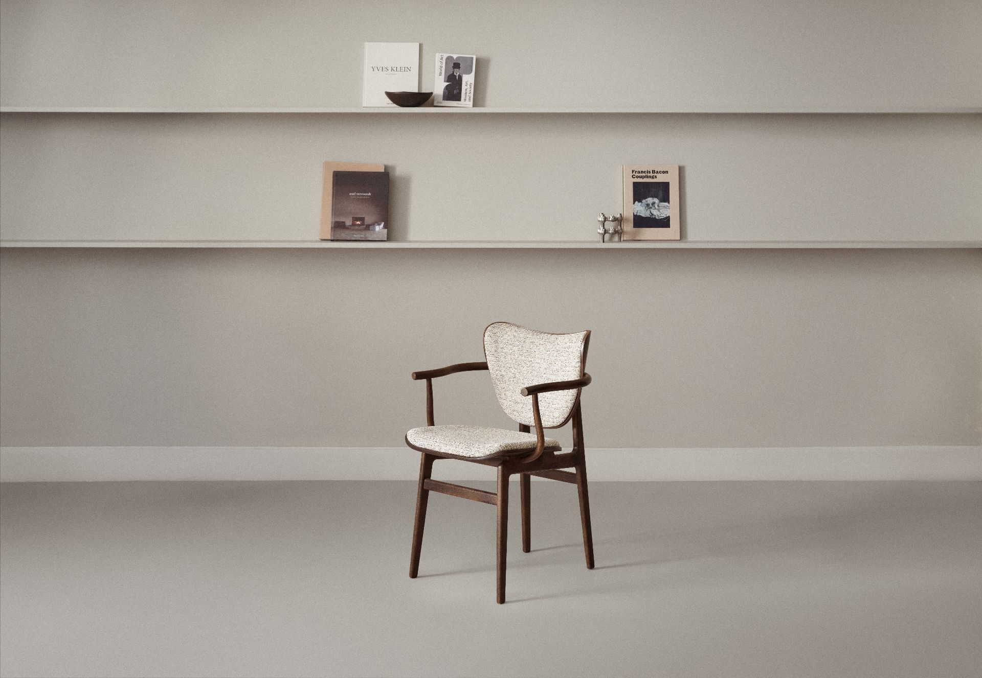 NORR11 Elephant Dining Armchair: Armlehnenstuhl aus dunklem Holz mit hell gemusterter Sitzfläche und Rückenlehne vor Regal.