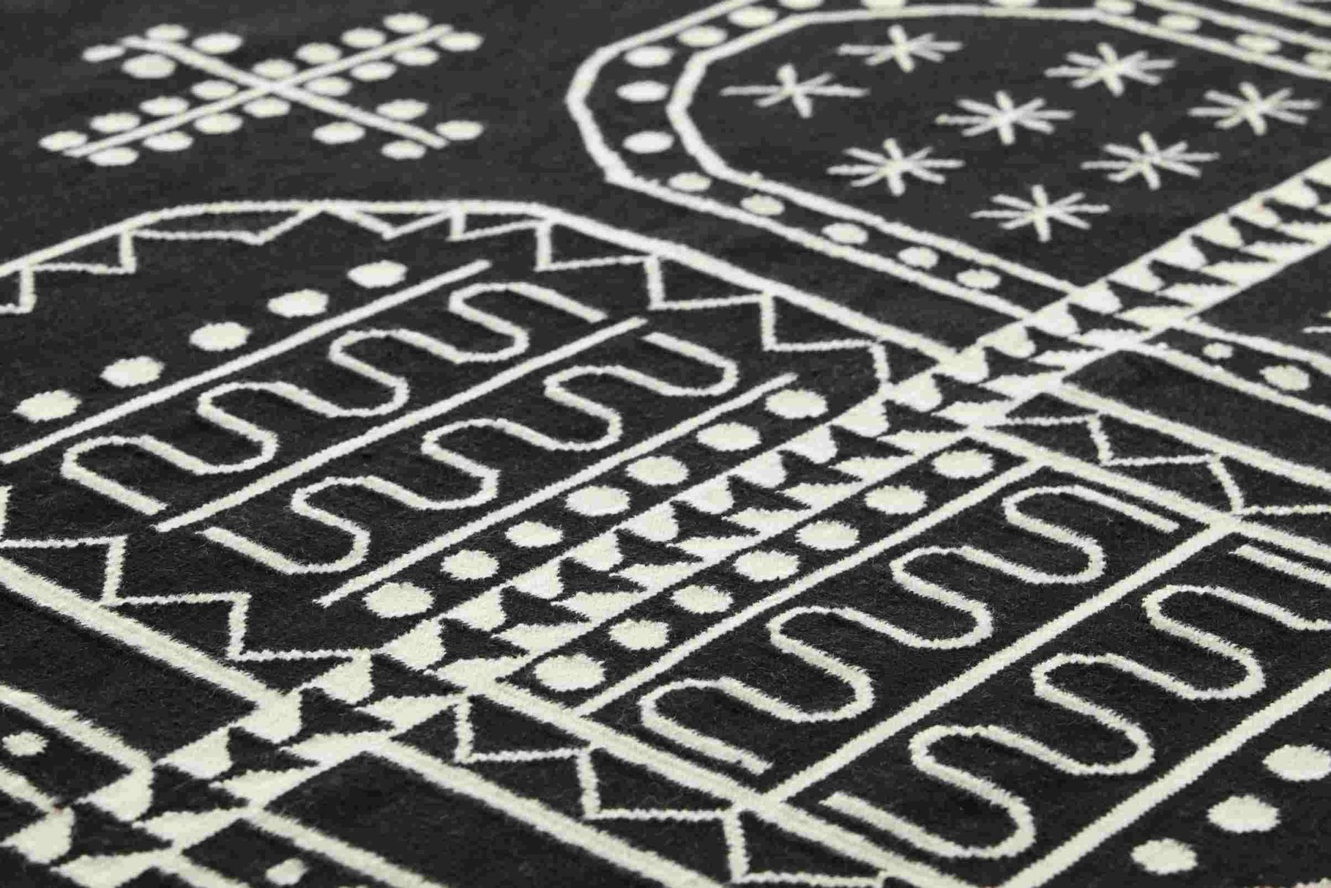 Detailaufnahme des Kilim Teppichs mit geometrischen, weißen Mustern auf schwarzem Grund.